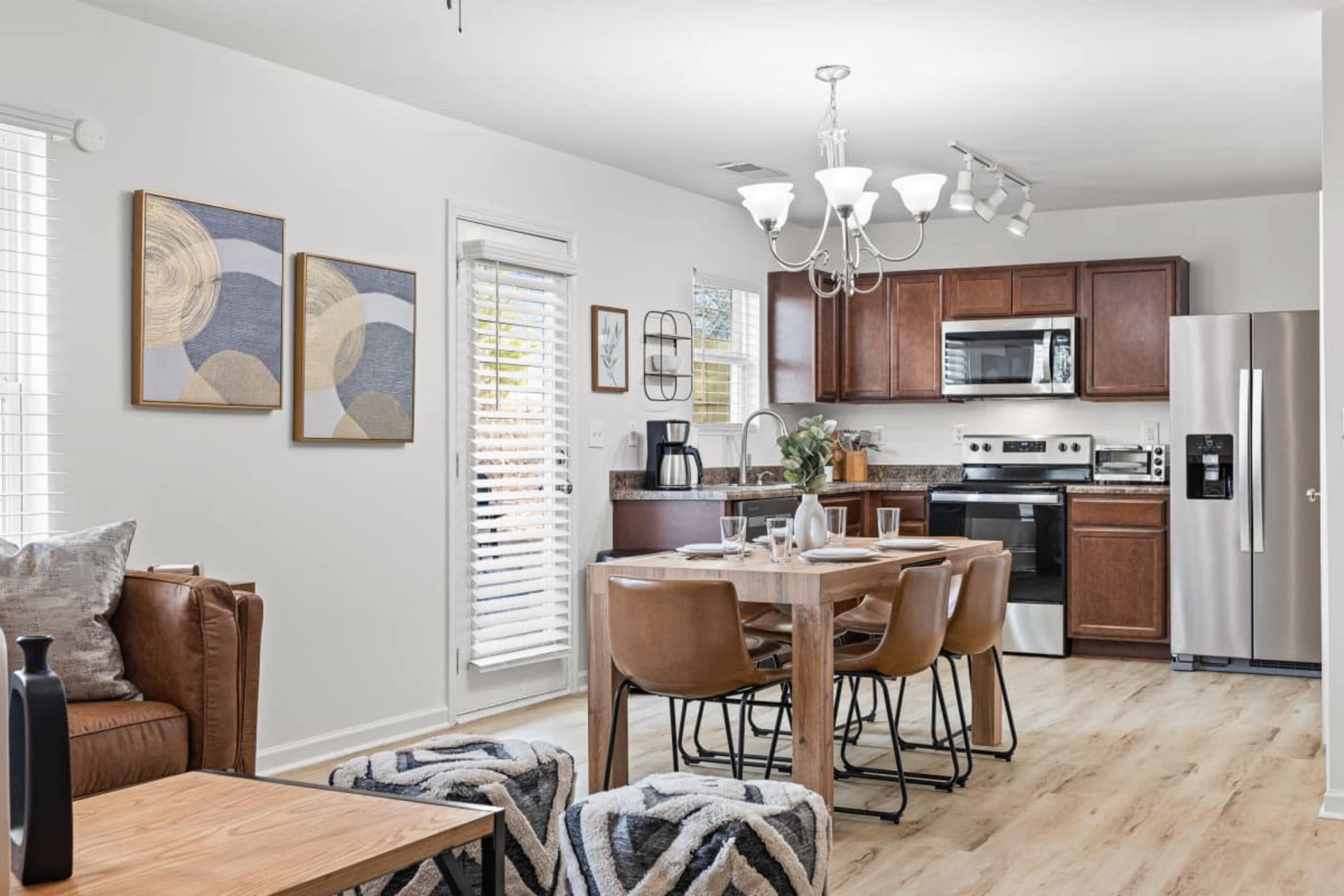 A modern kitchen and dining area featuring wooden cabinets, a stainless steel refrigerator, a dining table with brown chairs, and decorative wall art.
