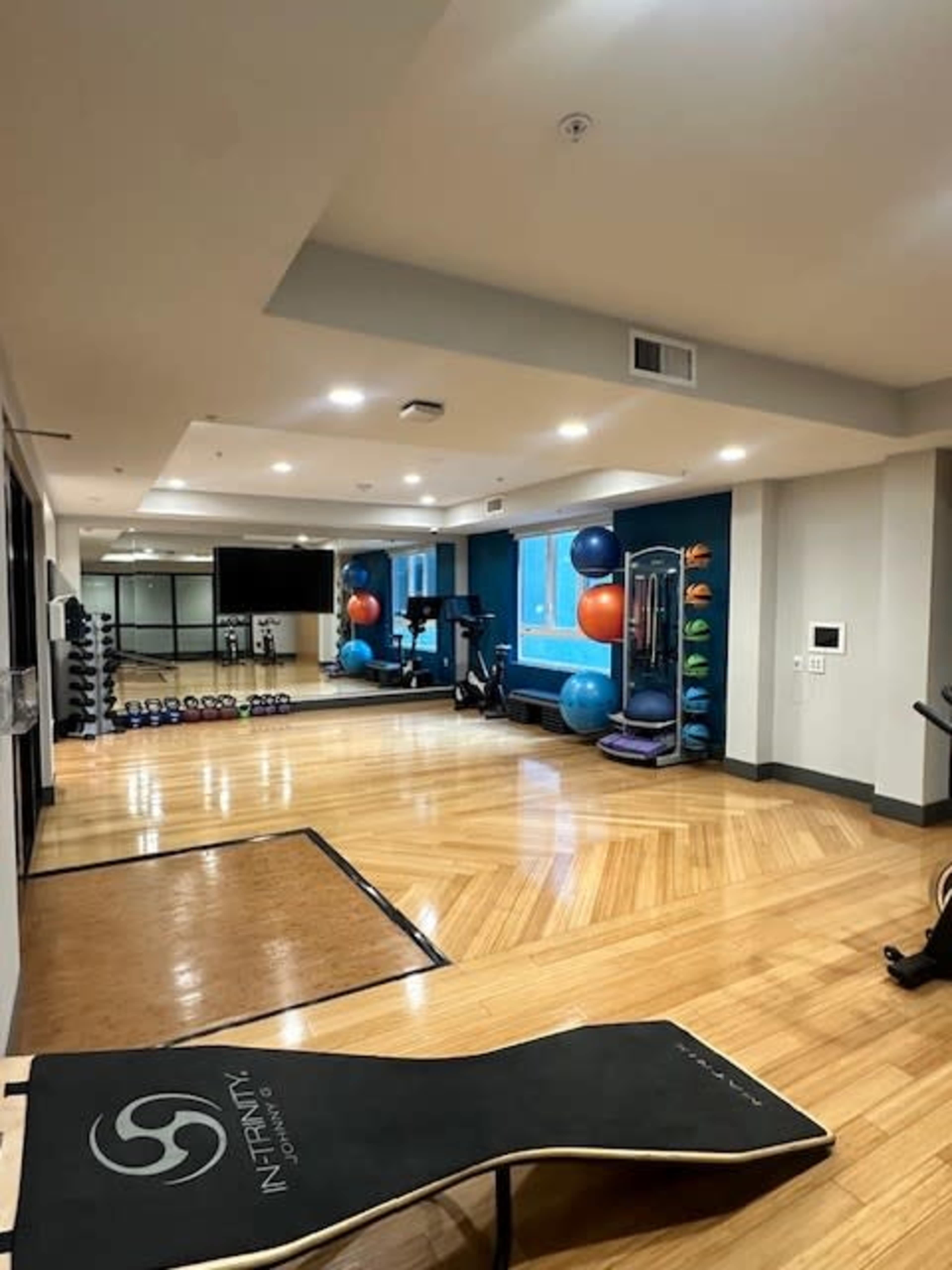 The image shows a spacious gym area featuring exercise equipment, free weights, stability balls, and mirrored walls.