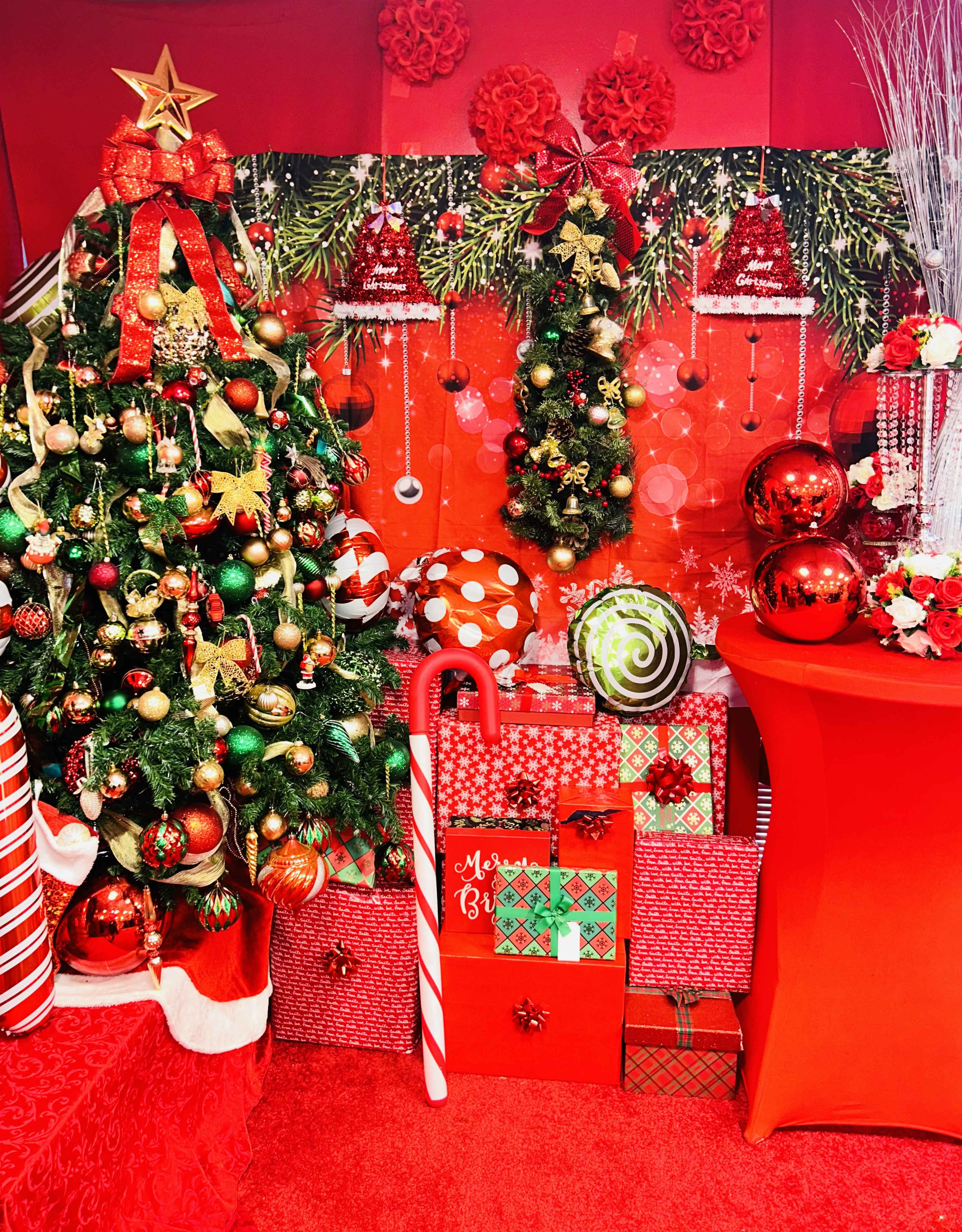 The scene features a decorated Christmas tree surrounded by colorful wrapped gifts, a candy cane, and festive ornaments against a red backdrop.