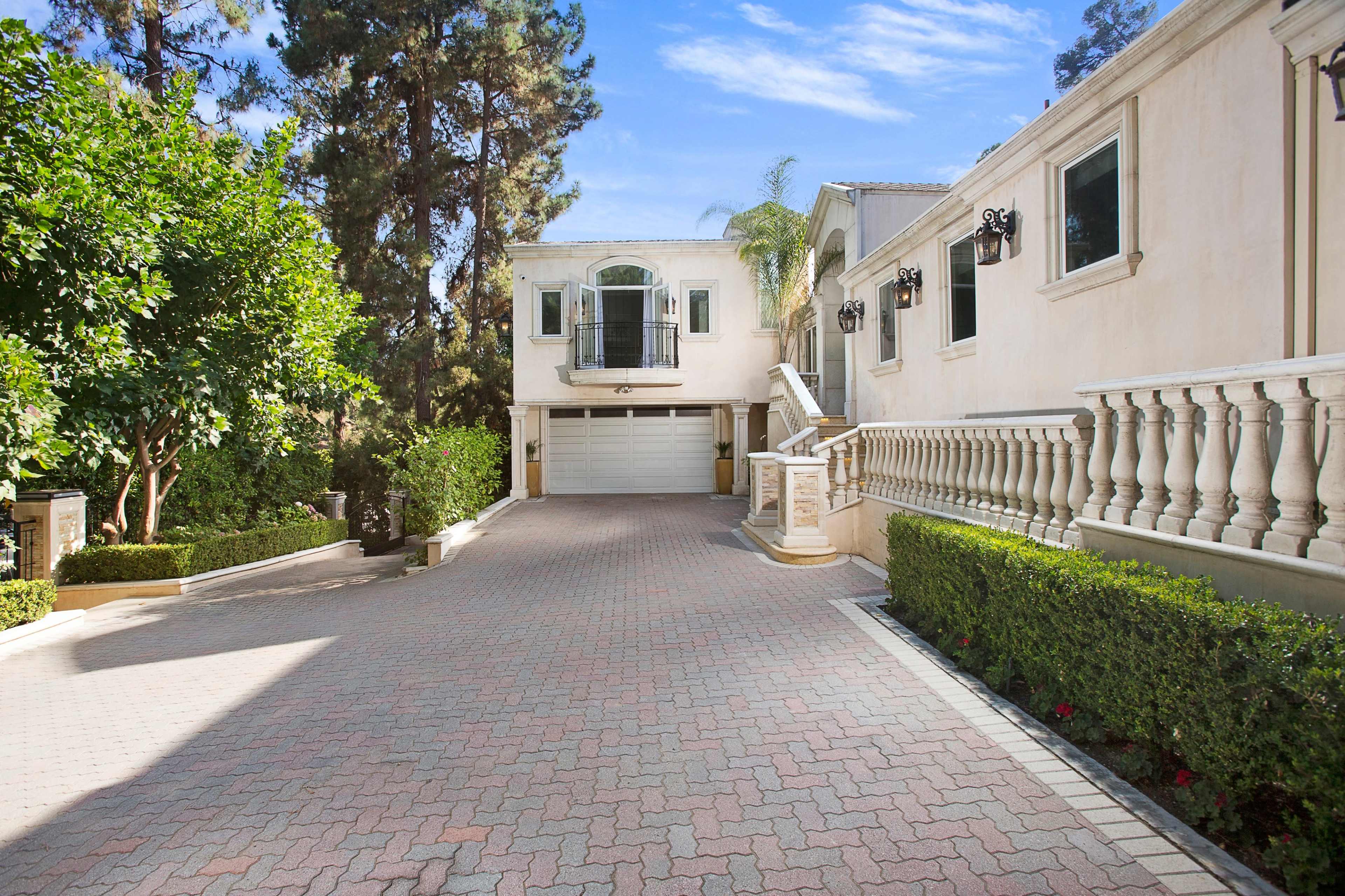 A spacious driveway leading to a large house with a garage and landscaped hedges on either side.