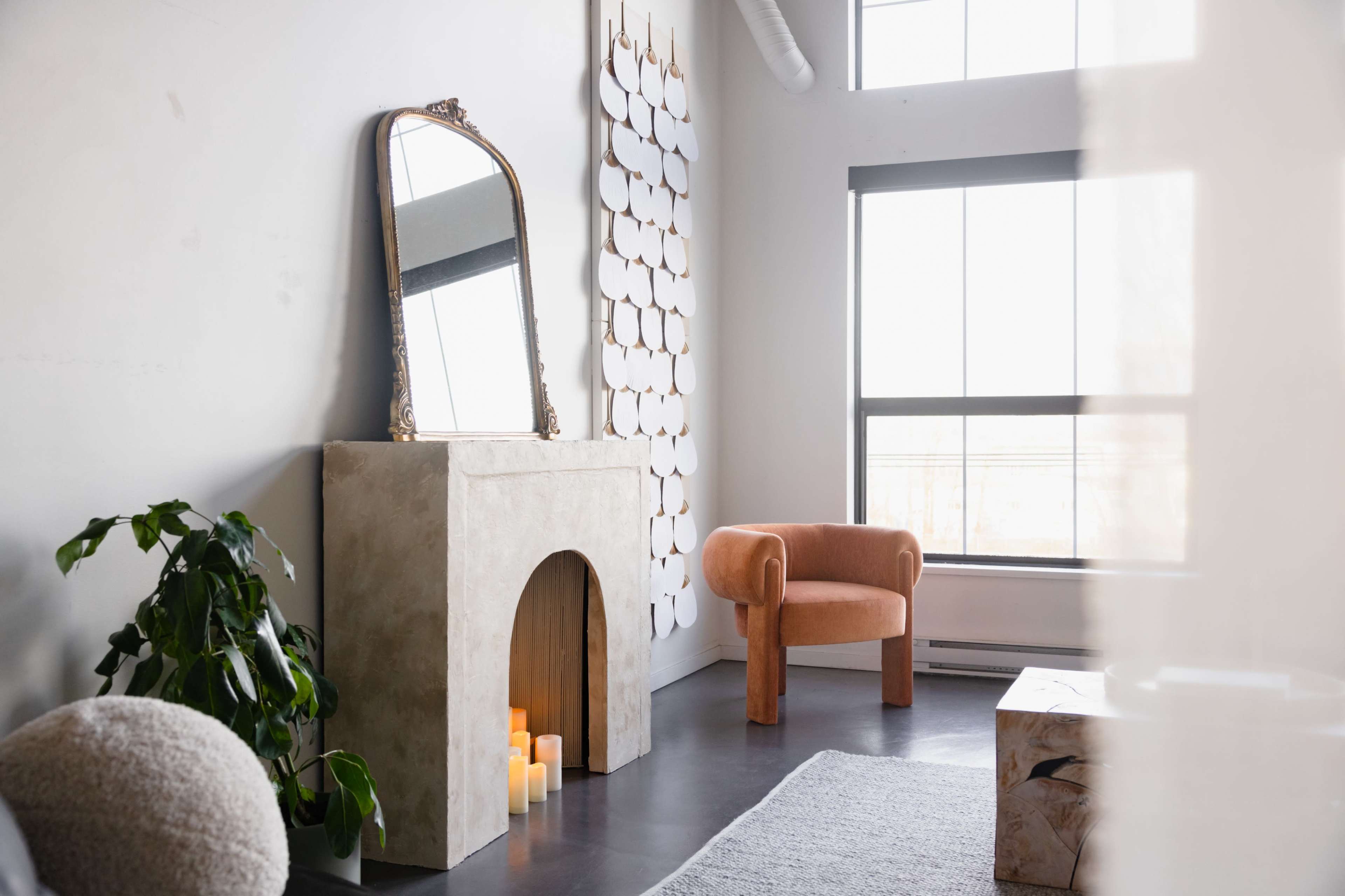 The image depicts a modern living room featuring a decorative fireplace with candles, an armchair, a large mirror, and a wall with abstract decor.