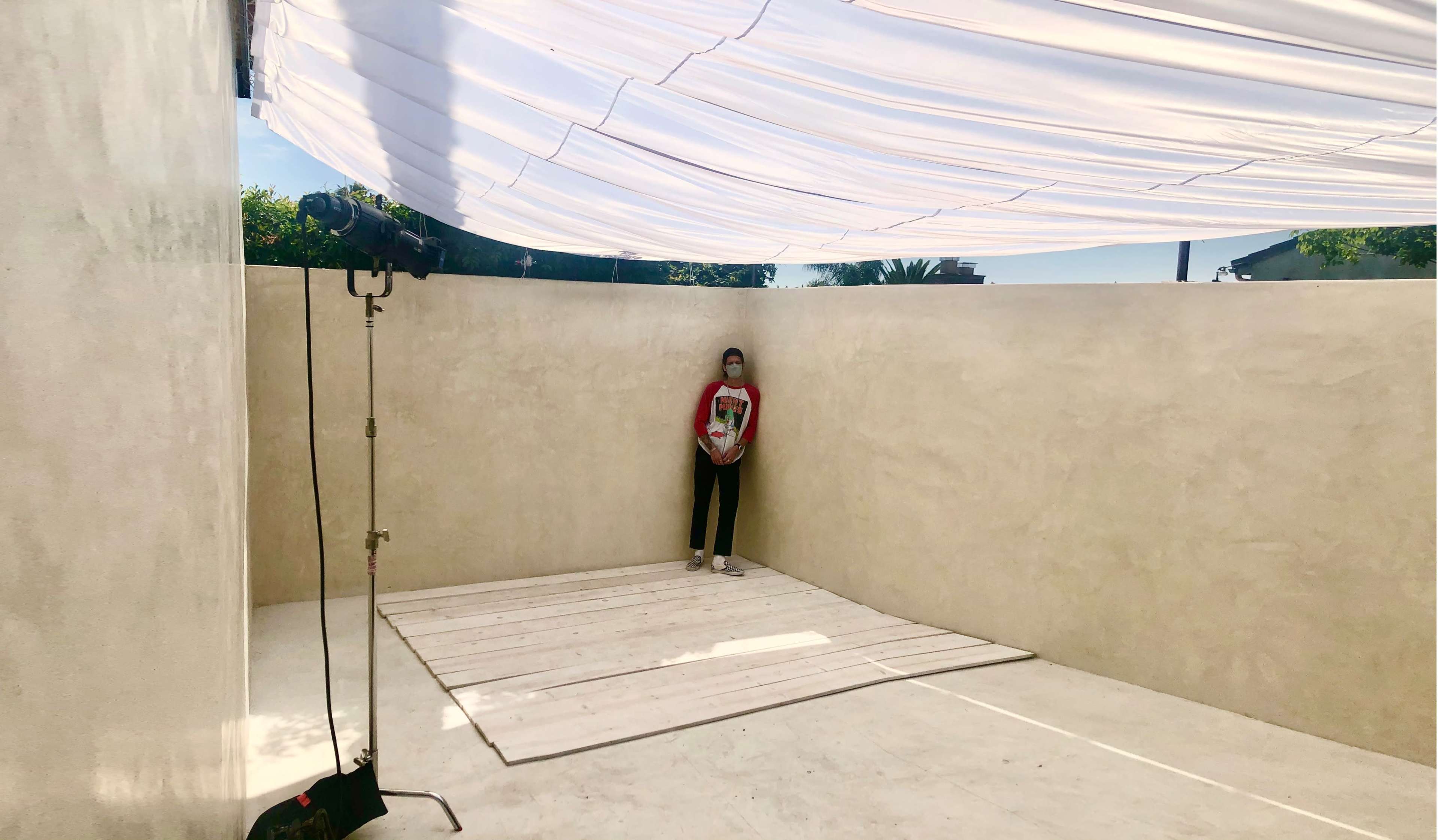 A person stands on a wooden platform in a minimally decorated outdoor space with a fabric canopy overhead.