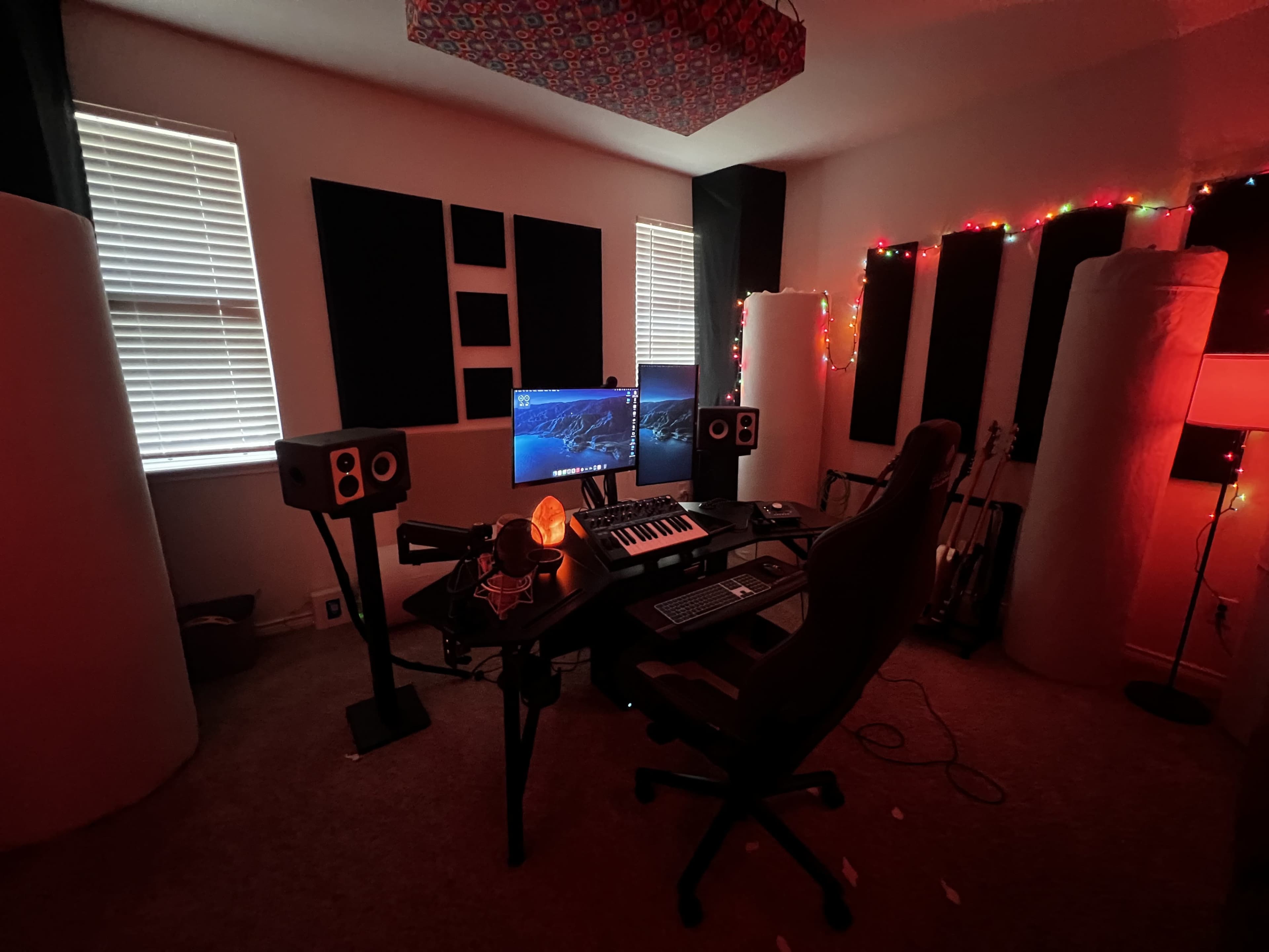 The image shows a music production studio with two computer monitors, a keyboard, speakers, and illuminated decor.