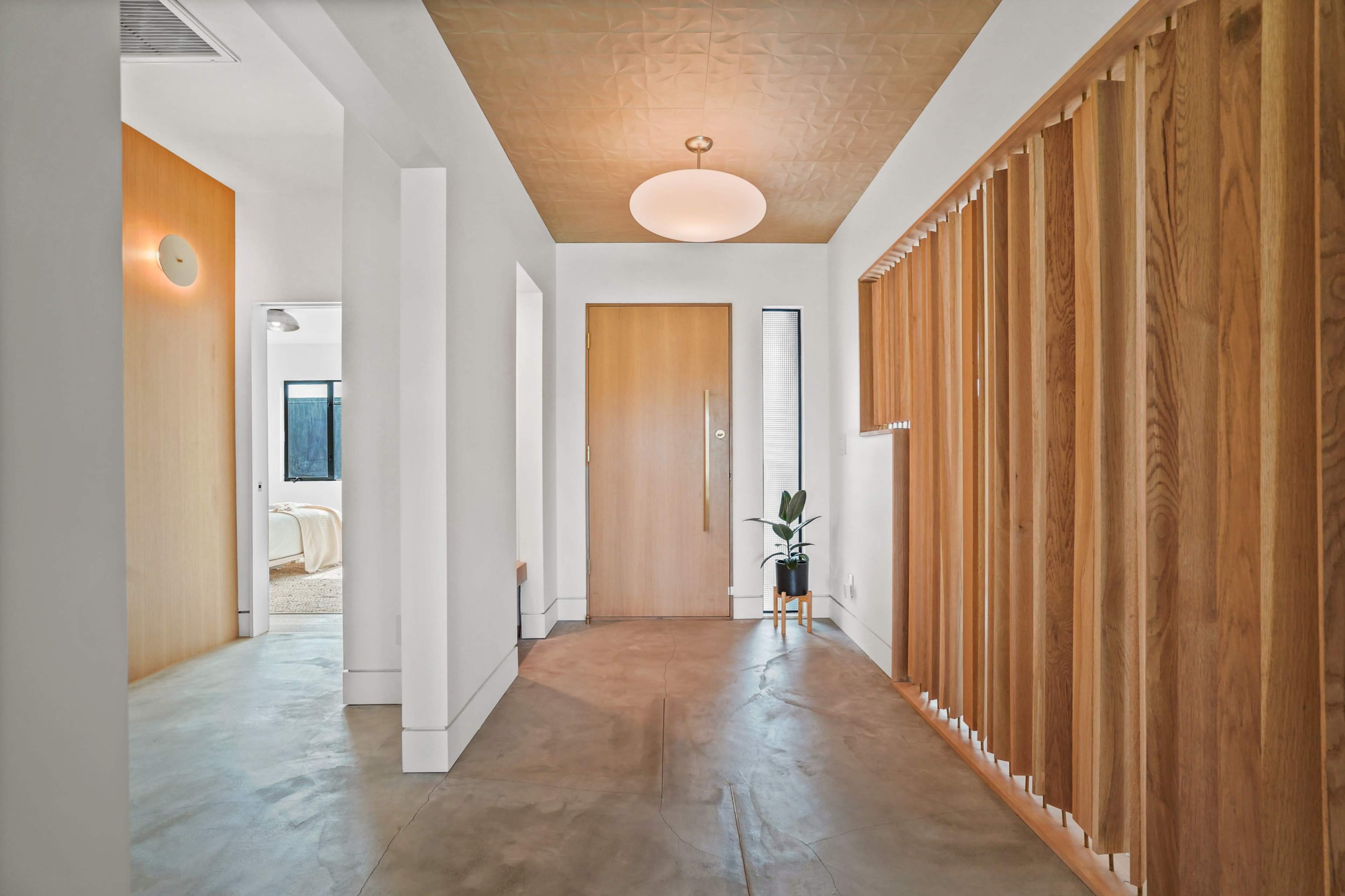 The image shows a modern hallway featuring a wooden accent wall, a light fixture, and a front door leading to another room.