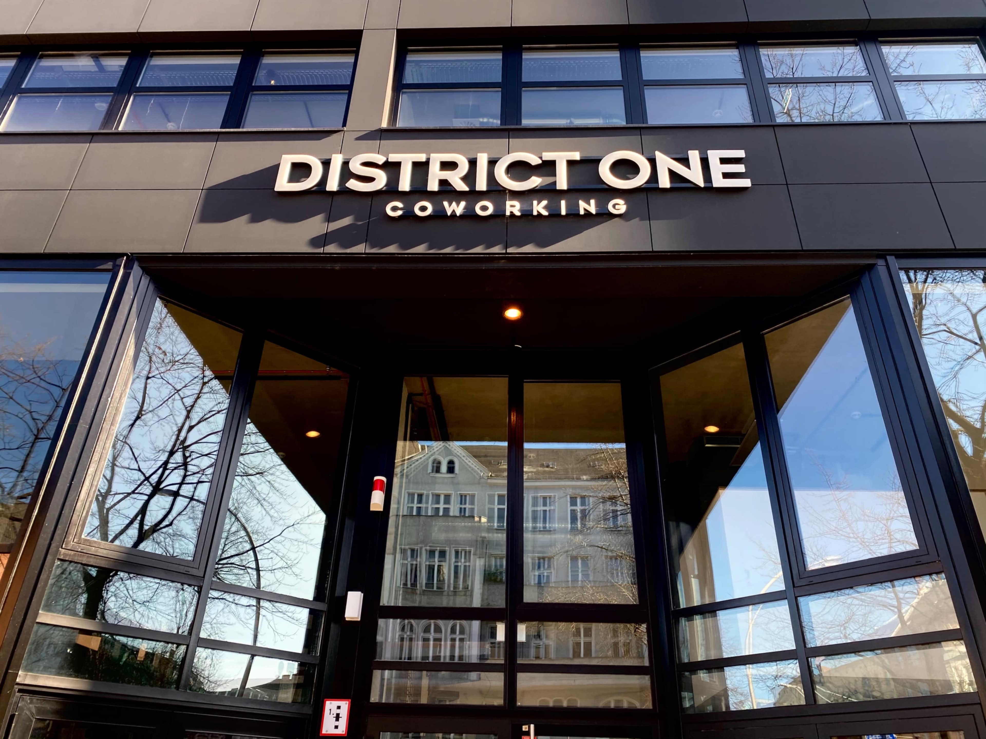 The entrance of a modern coworking space named "District One Coworking" features large glass doors and a sleek black facade.