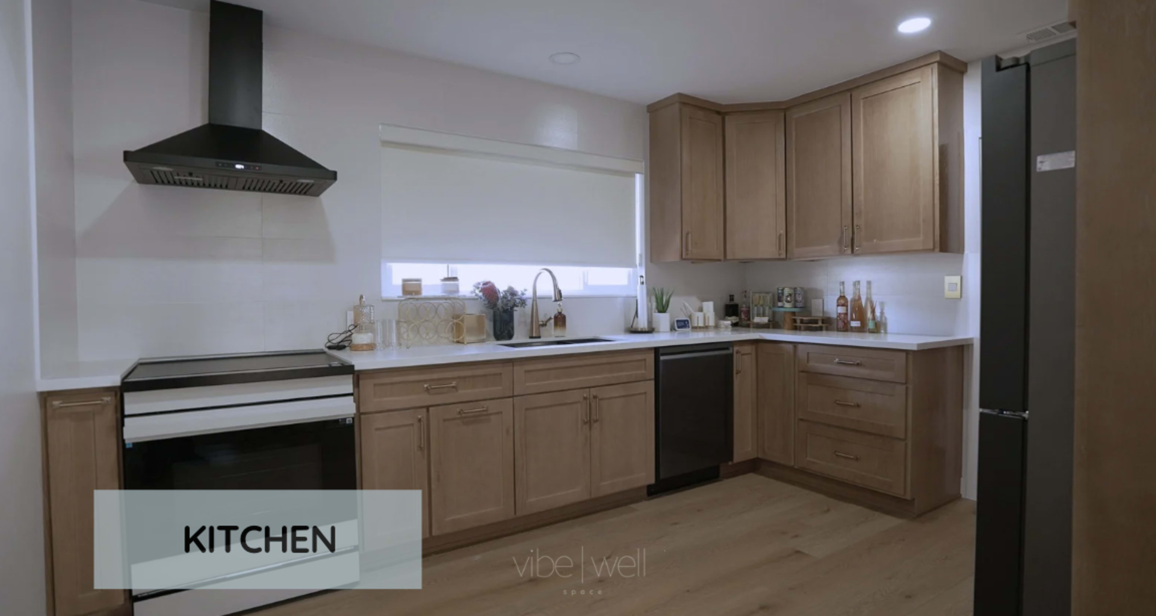 The image shows a modern kitchen with wooden cabinets, a white countertop, and stainless steel appliances.