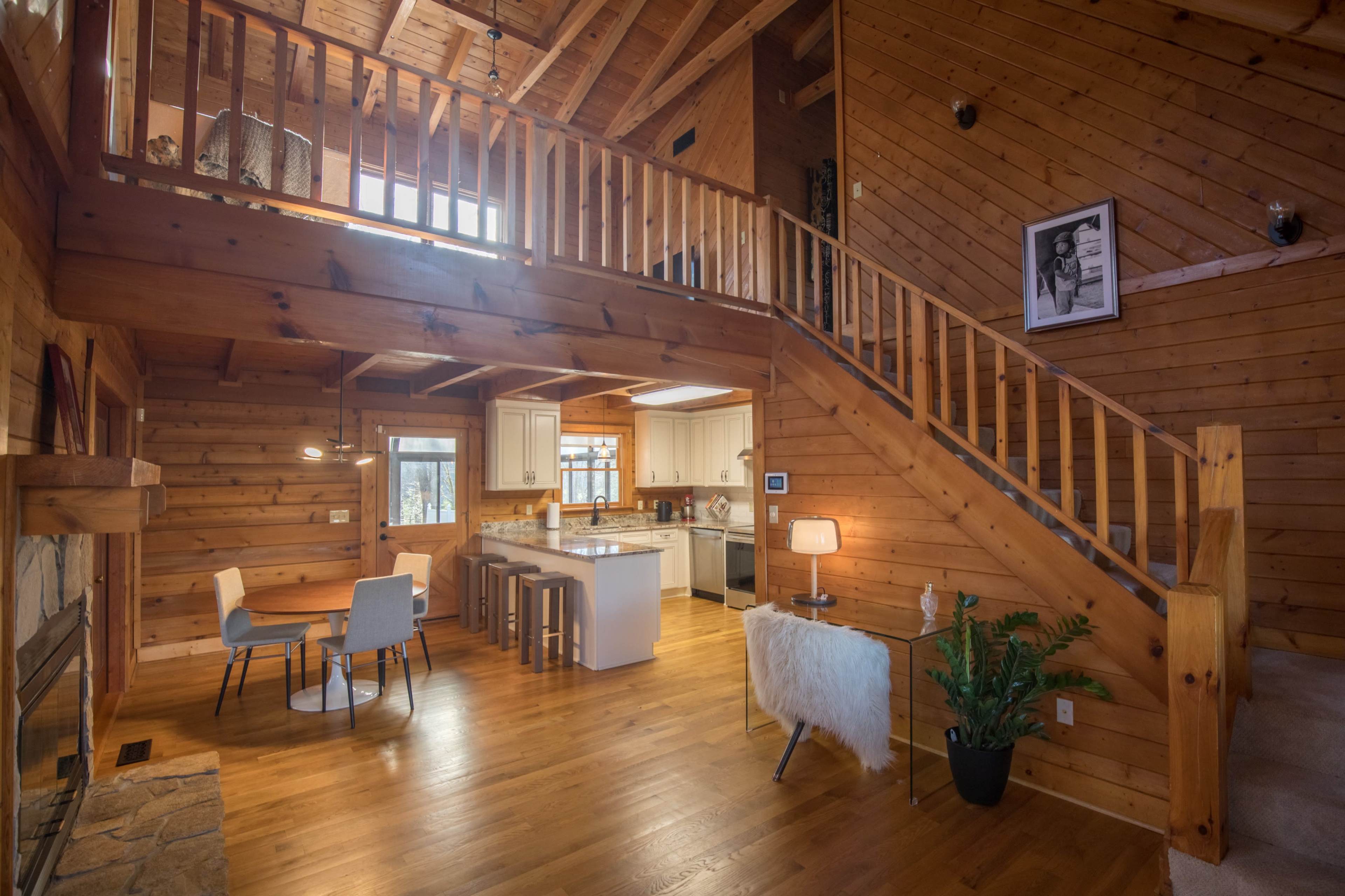 A wooden interior of a cabin featuring a staircase, a dining area with a table, and a kitchen area with an island.