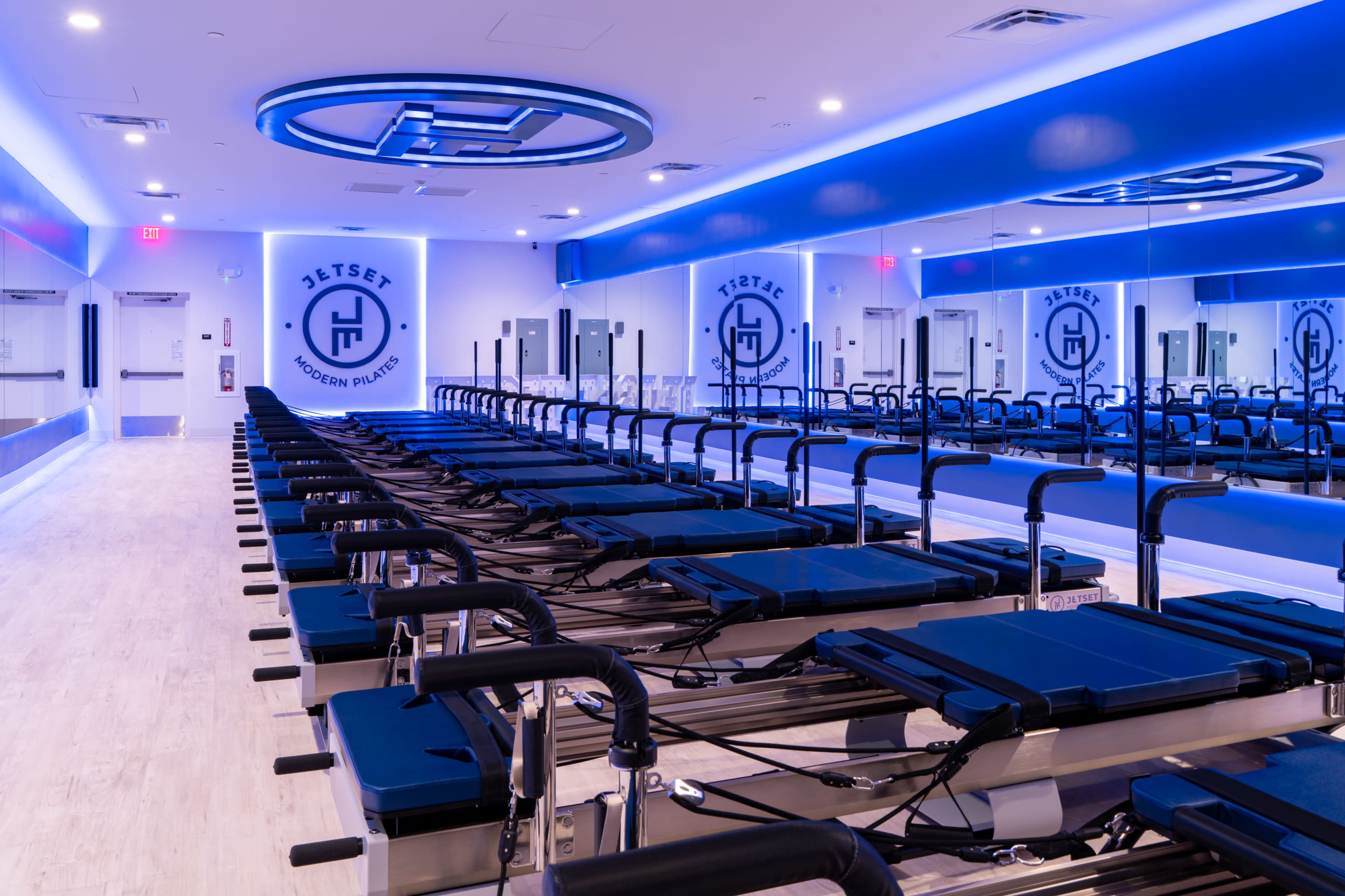 The image shows a modern fitness studio with several reformer machines arranged neatly in rows under blue lighting.