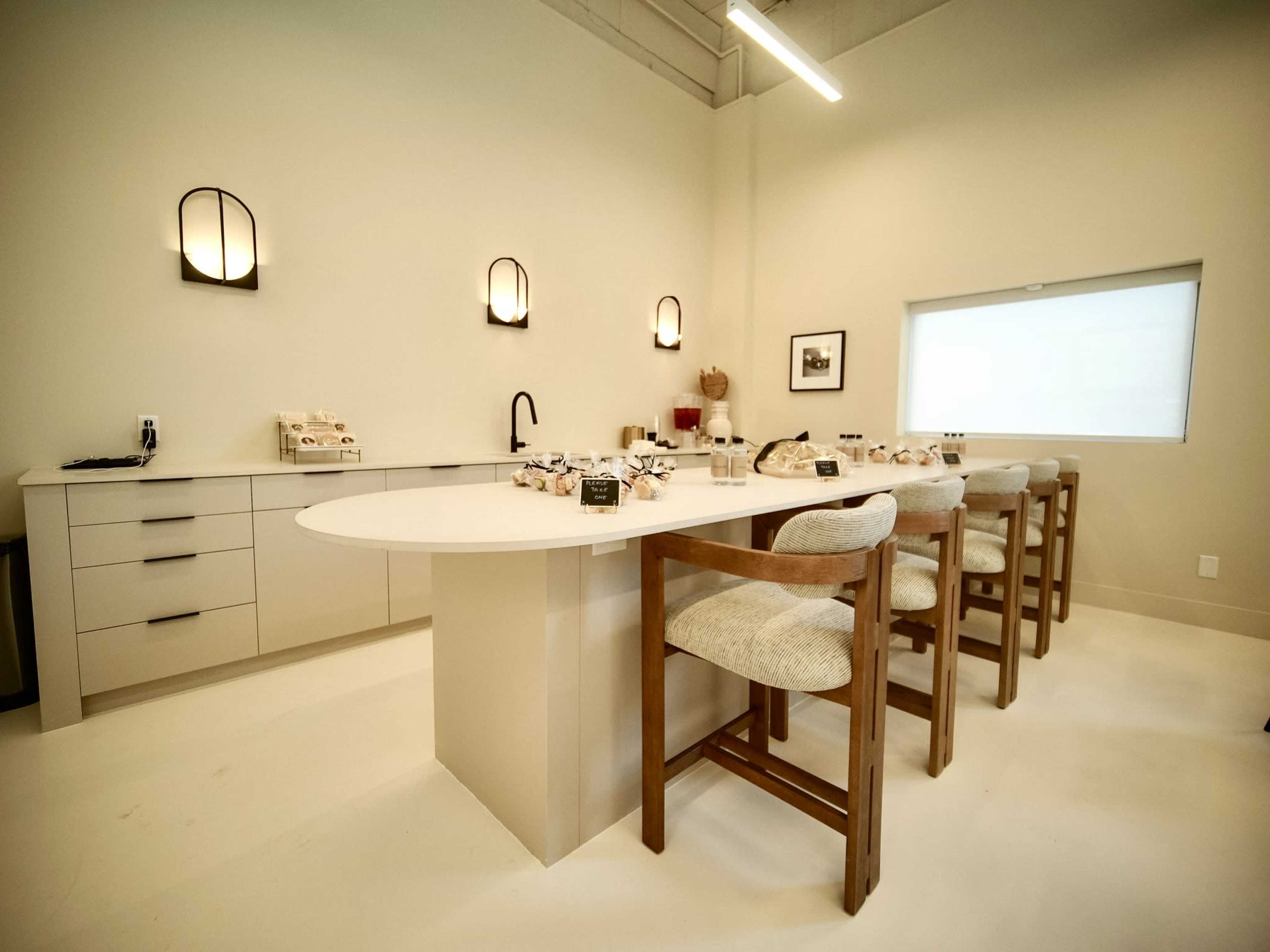 The image shows a modern kitchen with a large island and several bar stools, featuring minimalist cabinetry and wall-mounted light fixtures.