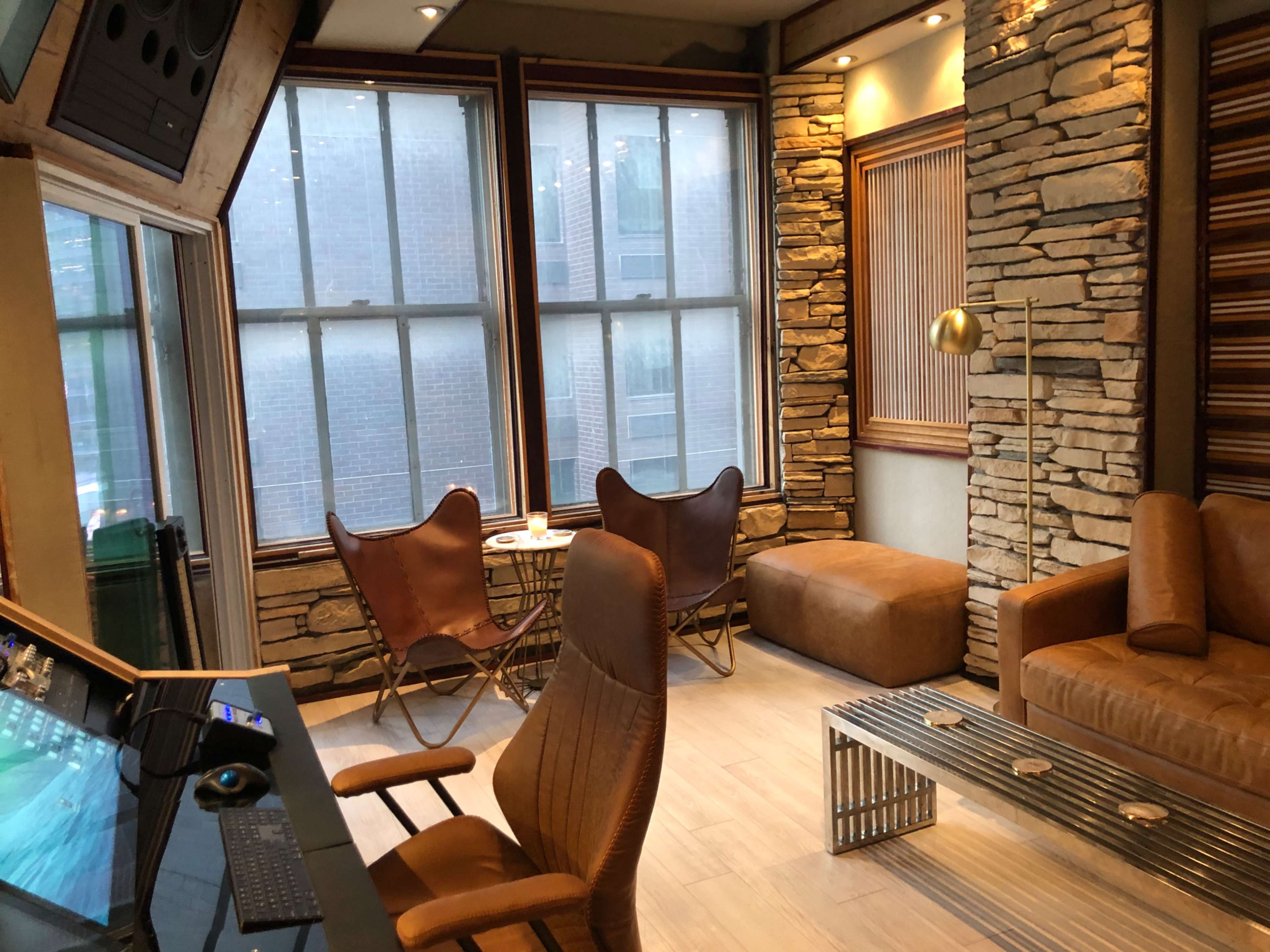 A modern room featuring two butterfly chairs, a sofa, a coffee table, and a workspace with a computer desk, all framed by large windows.