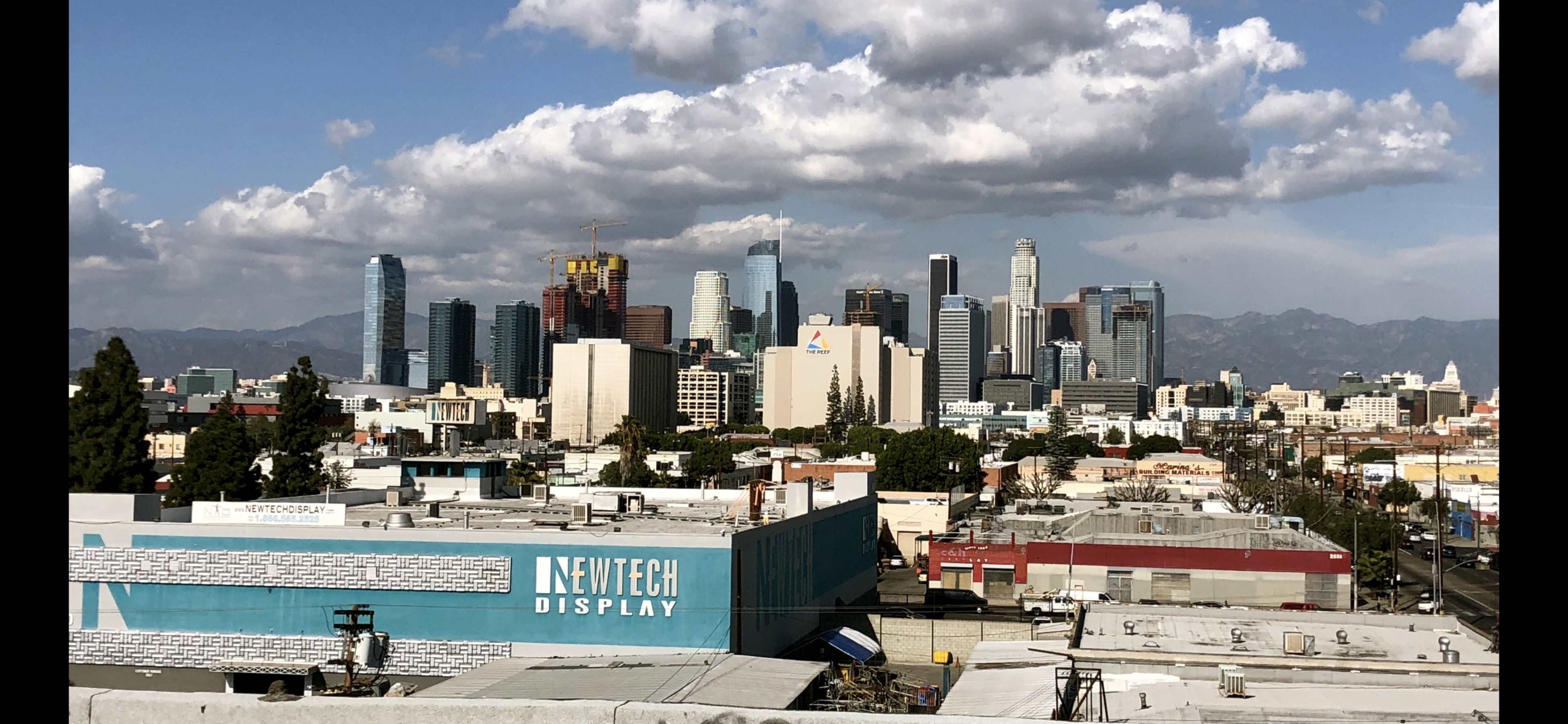 A skyline of Los Angeles with various skyscrapers and buildings under a partly cloudy sky.