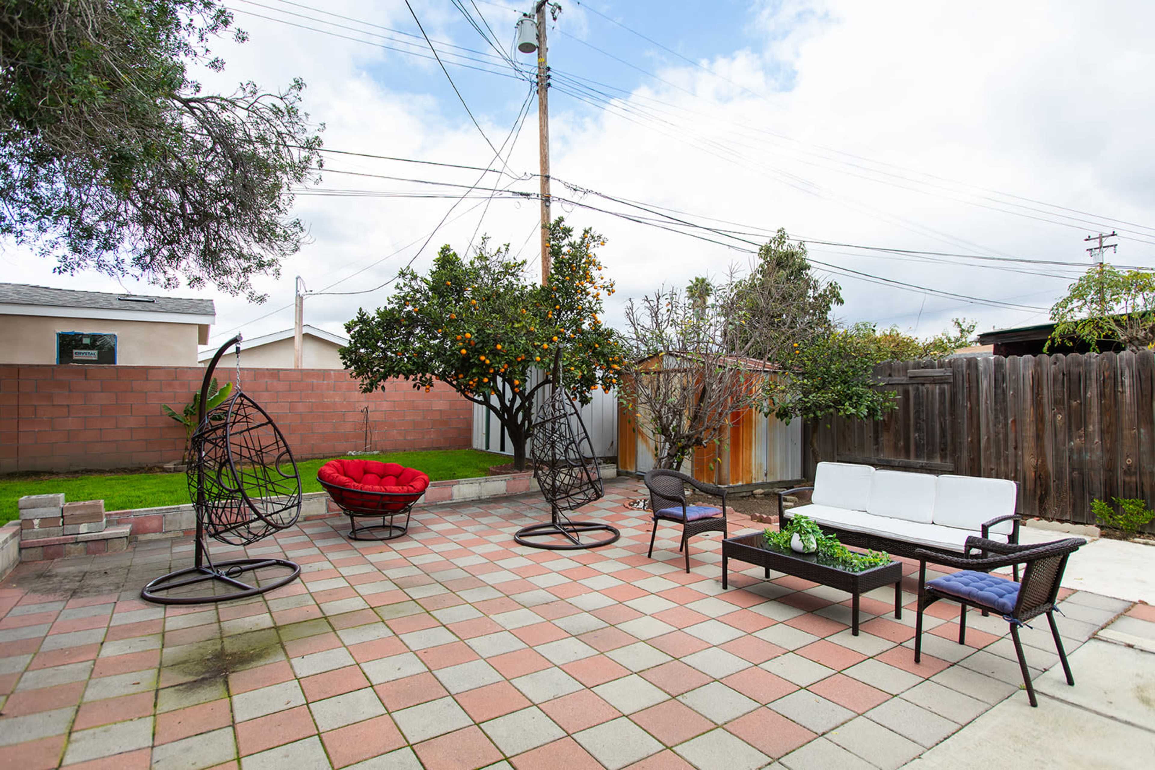 A backyard patio with hanging chairs, a seating area, and a couple of trees, including a citrus tree, surrounded by a tiled floor.
