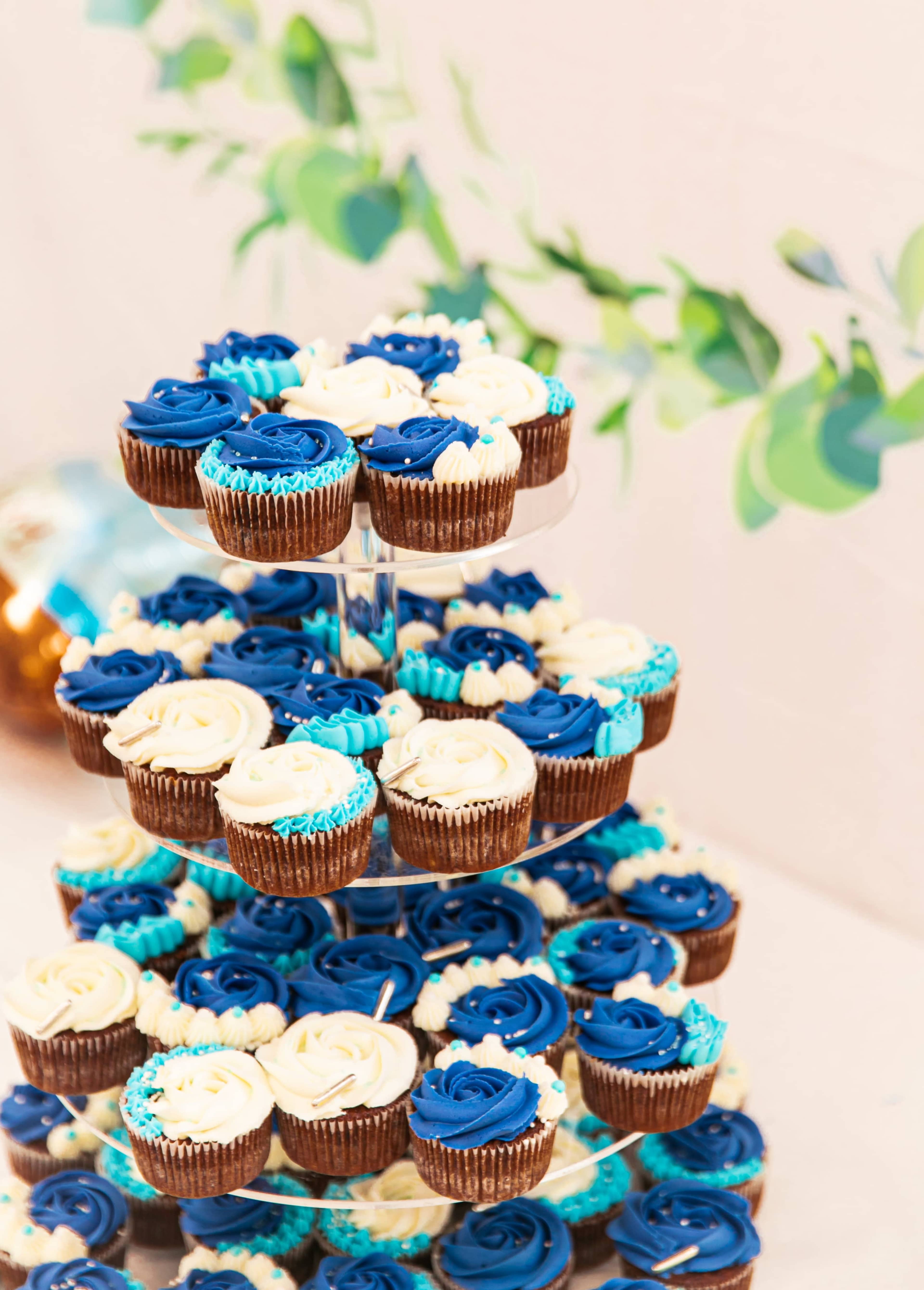 A tiered stand holds an array of blue and white frosted cupcakes.
