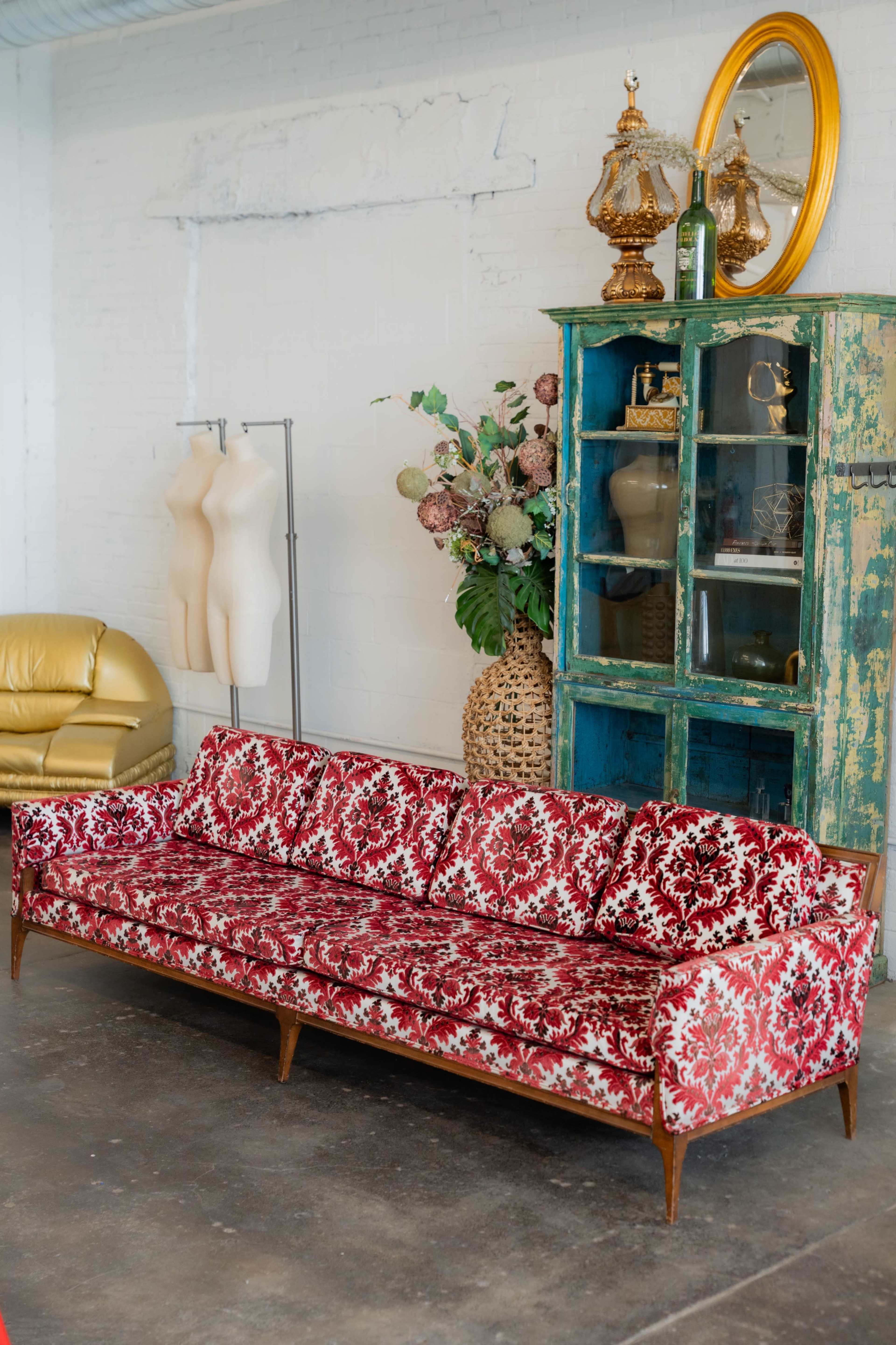 A red and white floral-patterned sofa is placed in a room with a green cabinet and decorative arrangements.