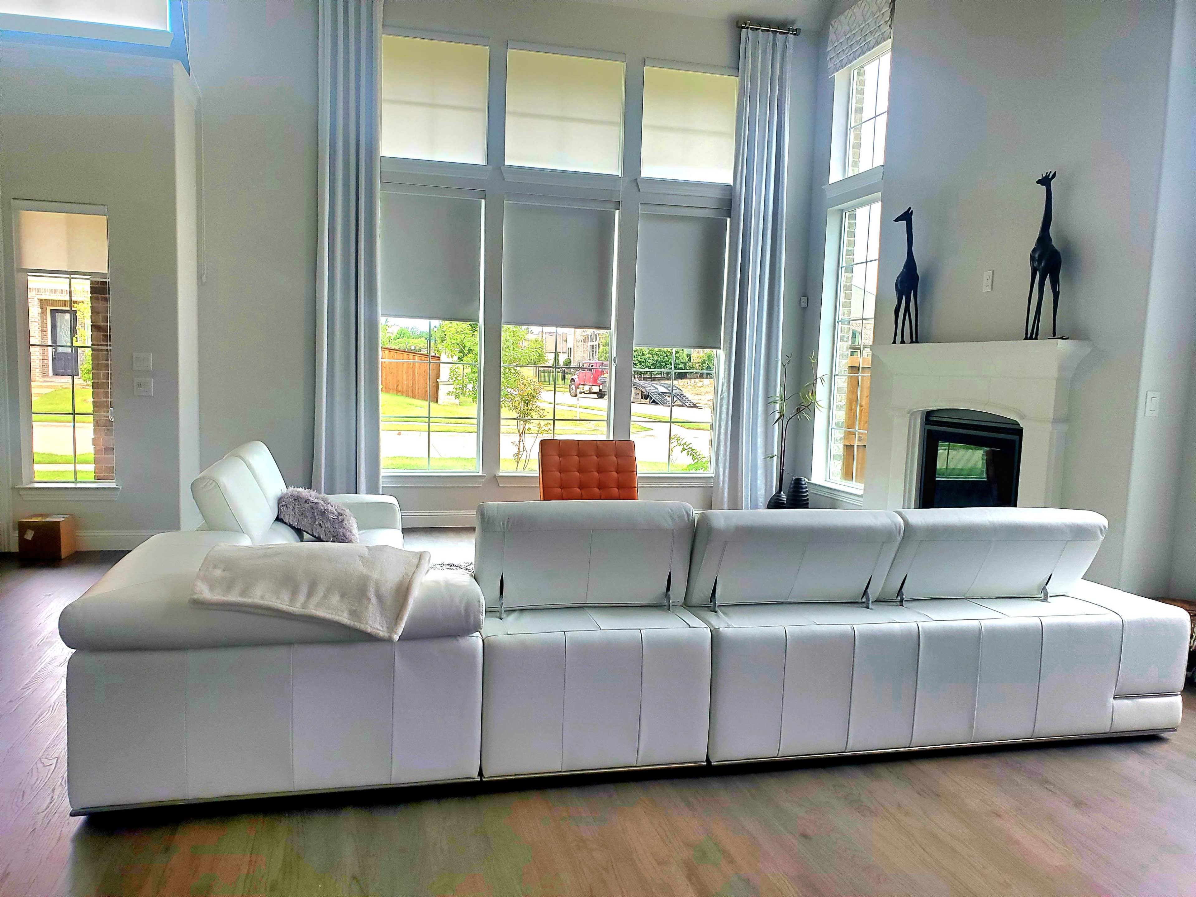 A modern living room features a spacious white sectional sofa facing a large window with vertical blinds and a white fireplace.