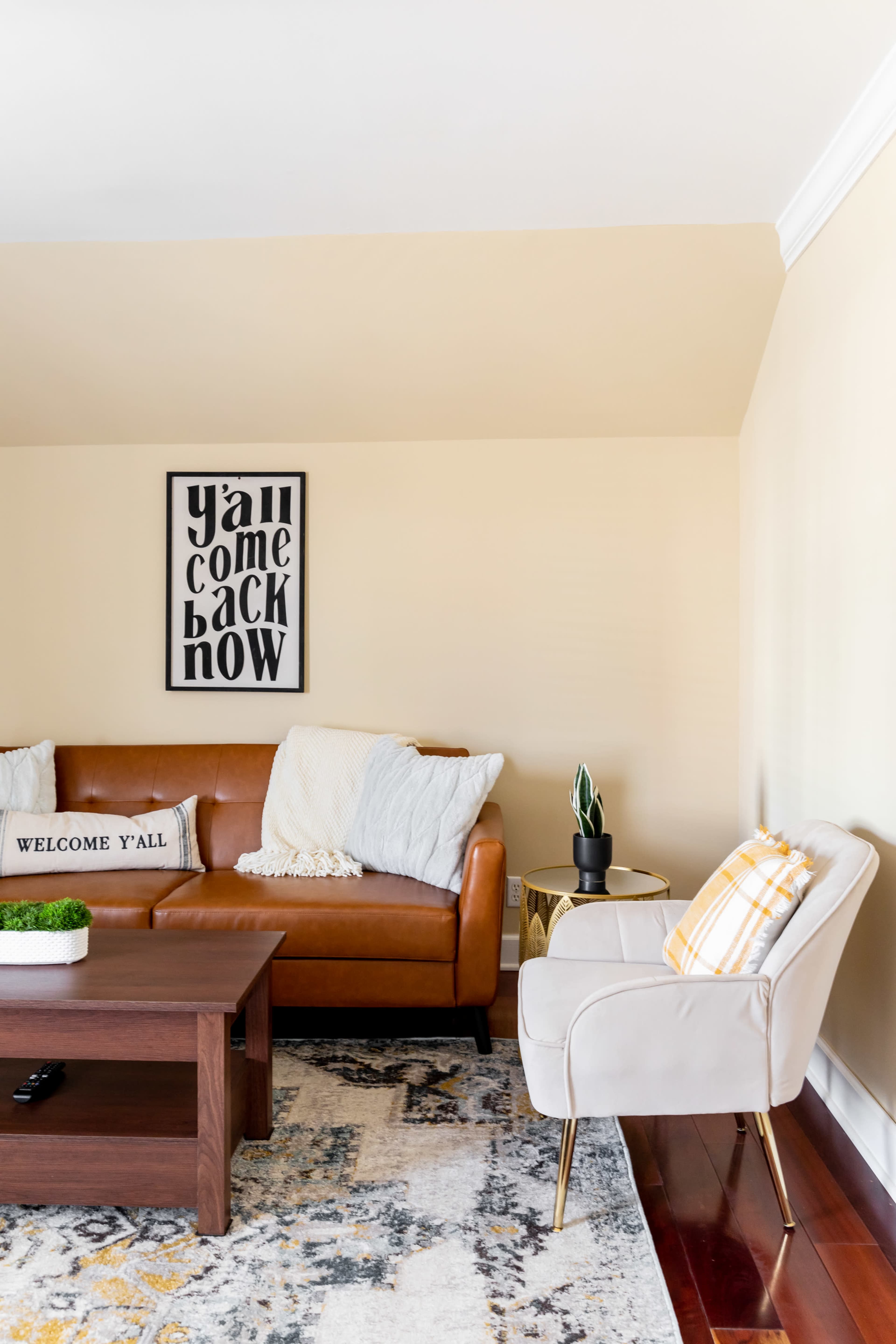 A living room with a brown leather sofa, a wooden coffee table, a decorative chair, and a large area rug.
