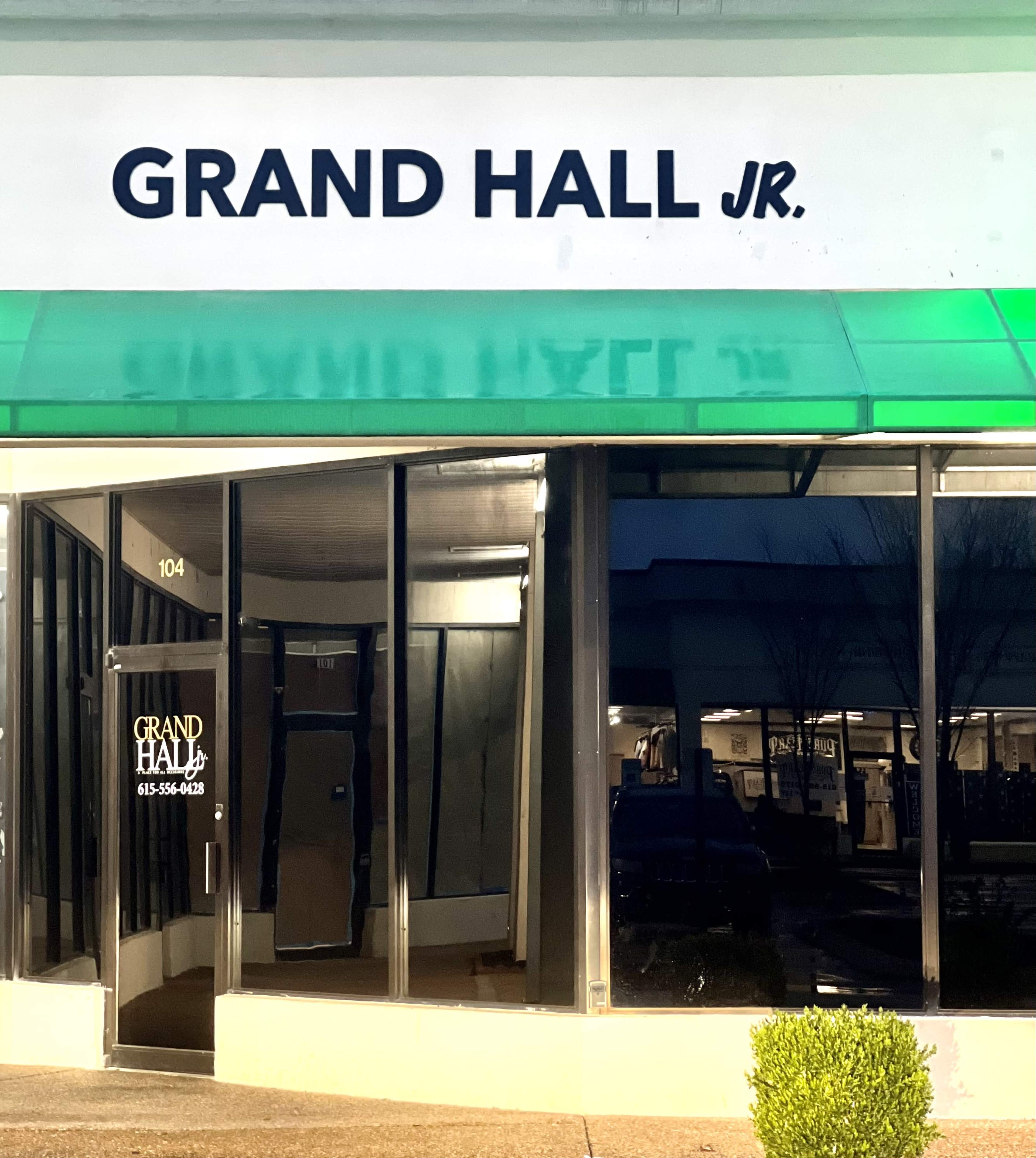 The image shows the exterior of a storefront labeled "GRAND HALL JR." with large glass windows and a green awning.