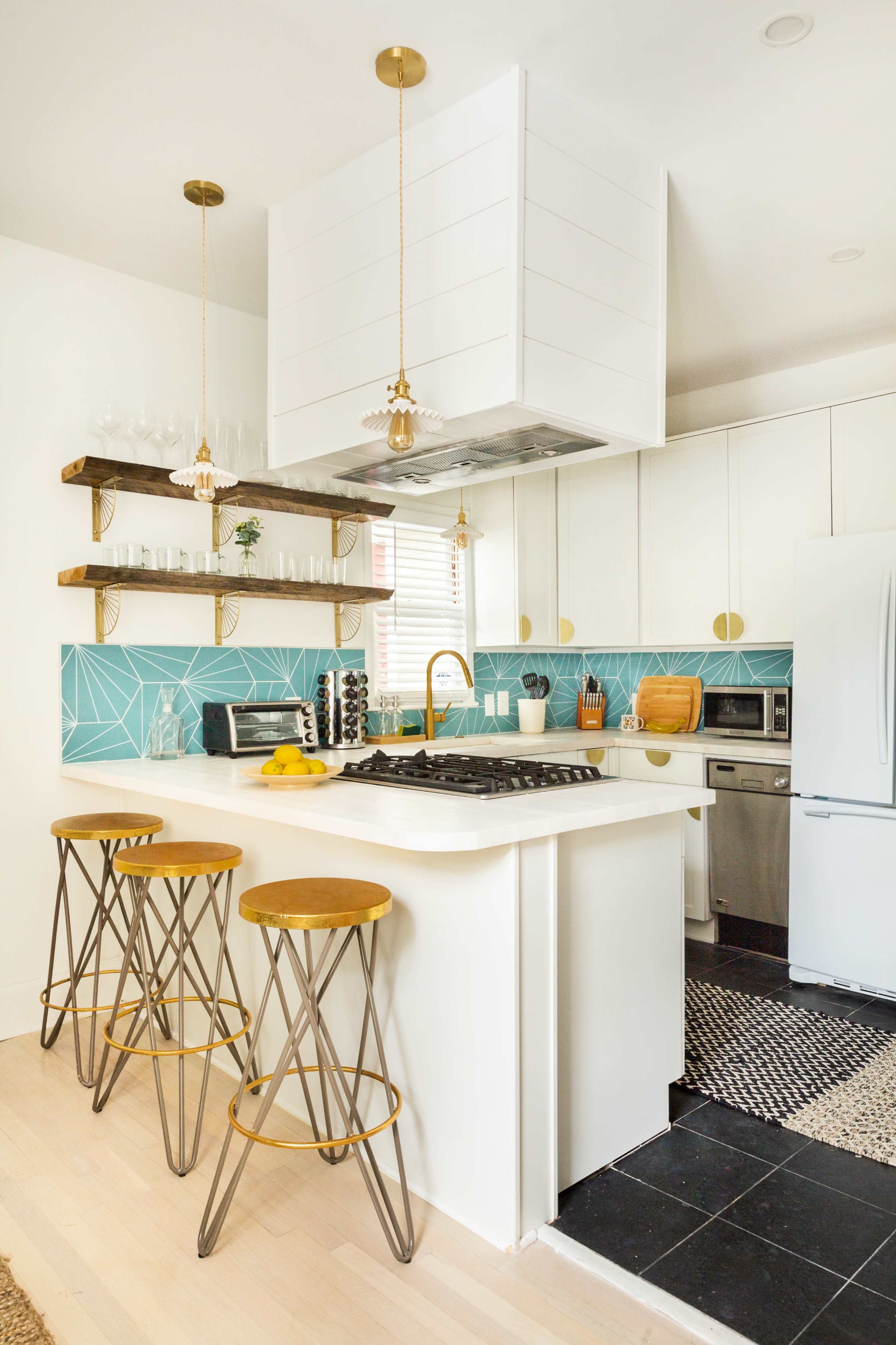 A modern kitchen features a white island with three stools, a turquoise tile backsplash, open shelving, and stainless steel appliances.