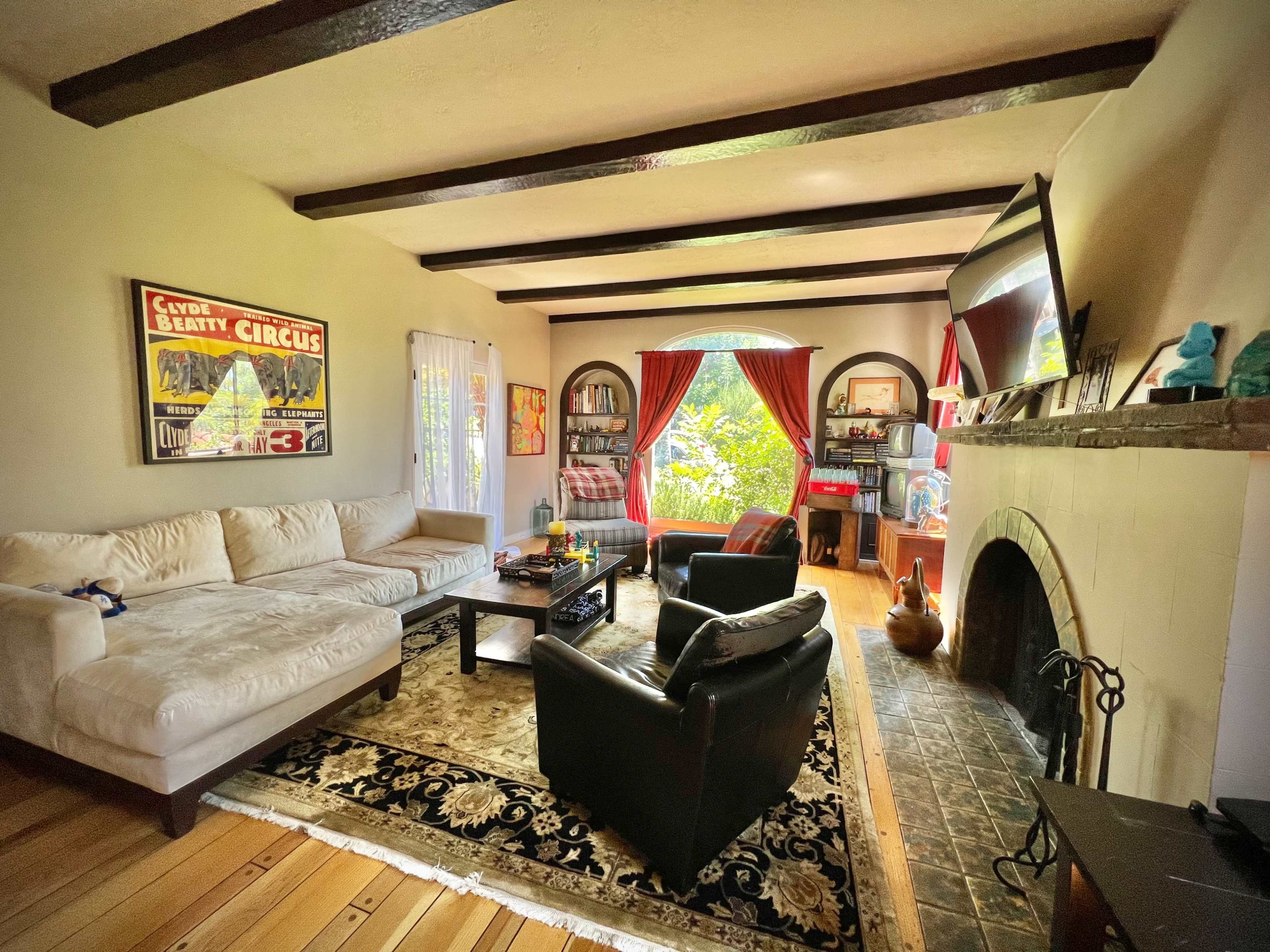 The living room features a sectional sofa, a coffee table, and armchairs arranged around a fireplace, with large windows allowing natural light to enter.