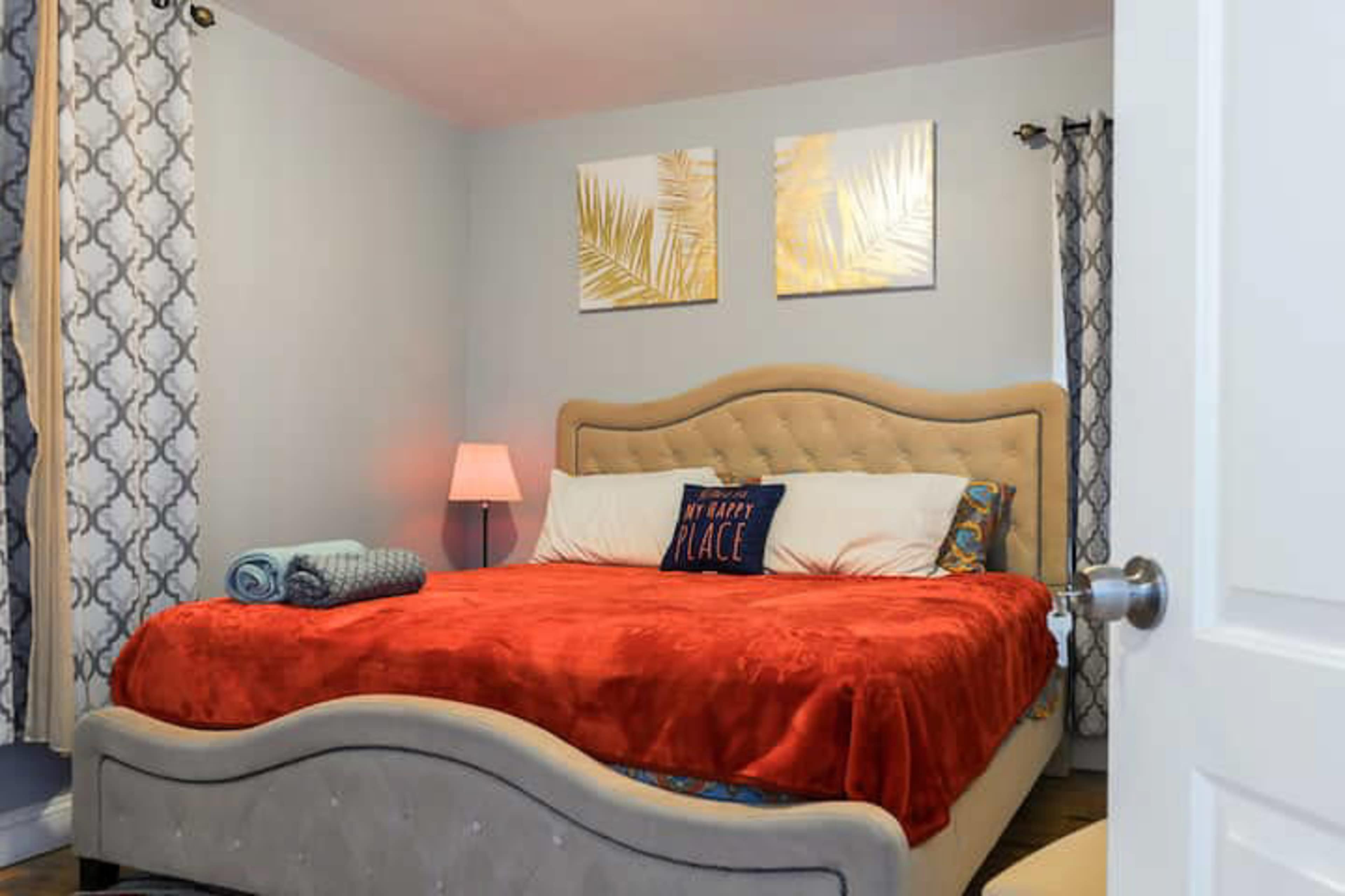A neatly arranged bedroom features a bed with a red blanket, decorative pillows, and two framed artworks on the walls.