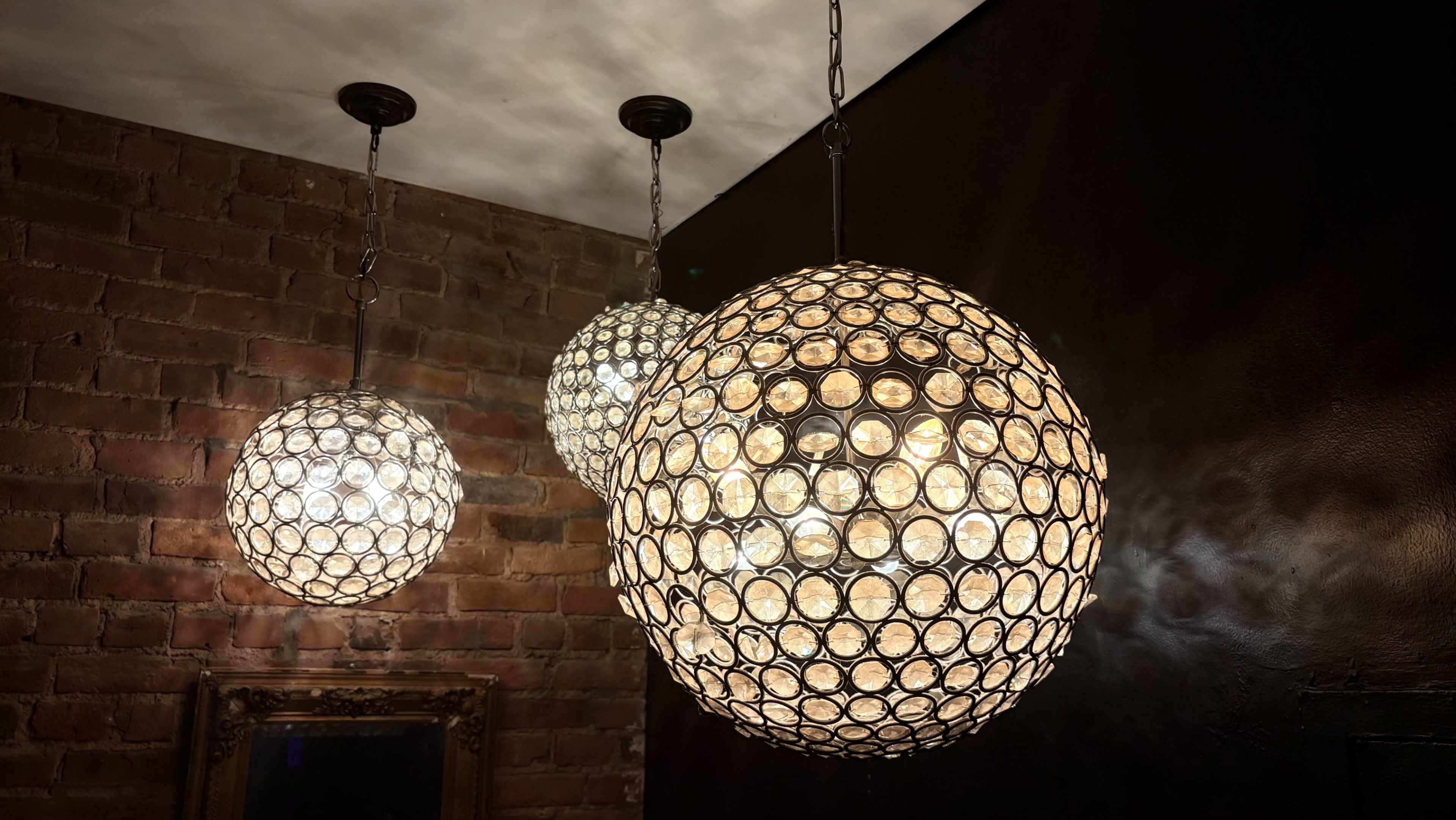 Three spherical pendant lights hang from a ceiling with a textured dark wall and exposed brick.