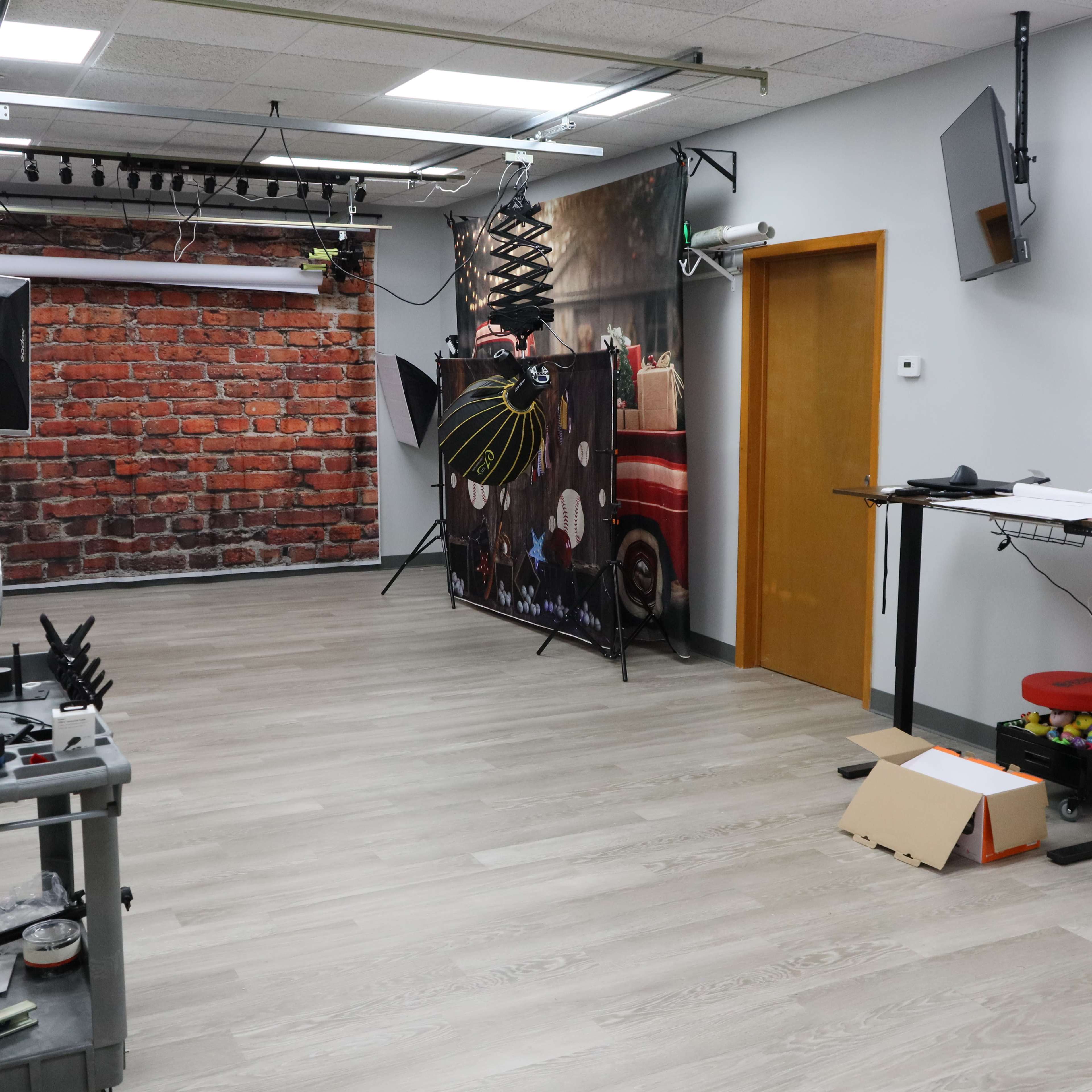The image shows a studio space with brick-patterned and themed backdrops, lighting equipment, and a doorway leading to another area.