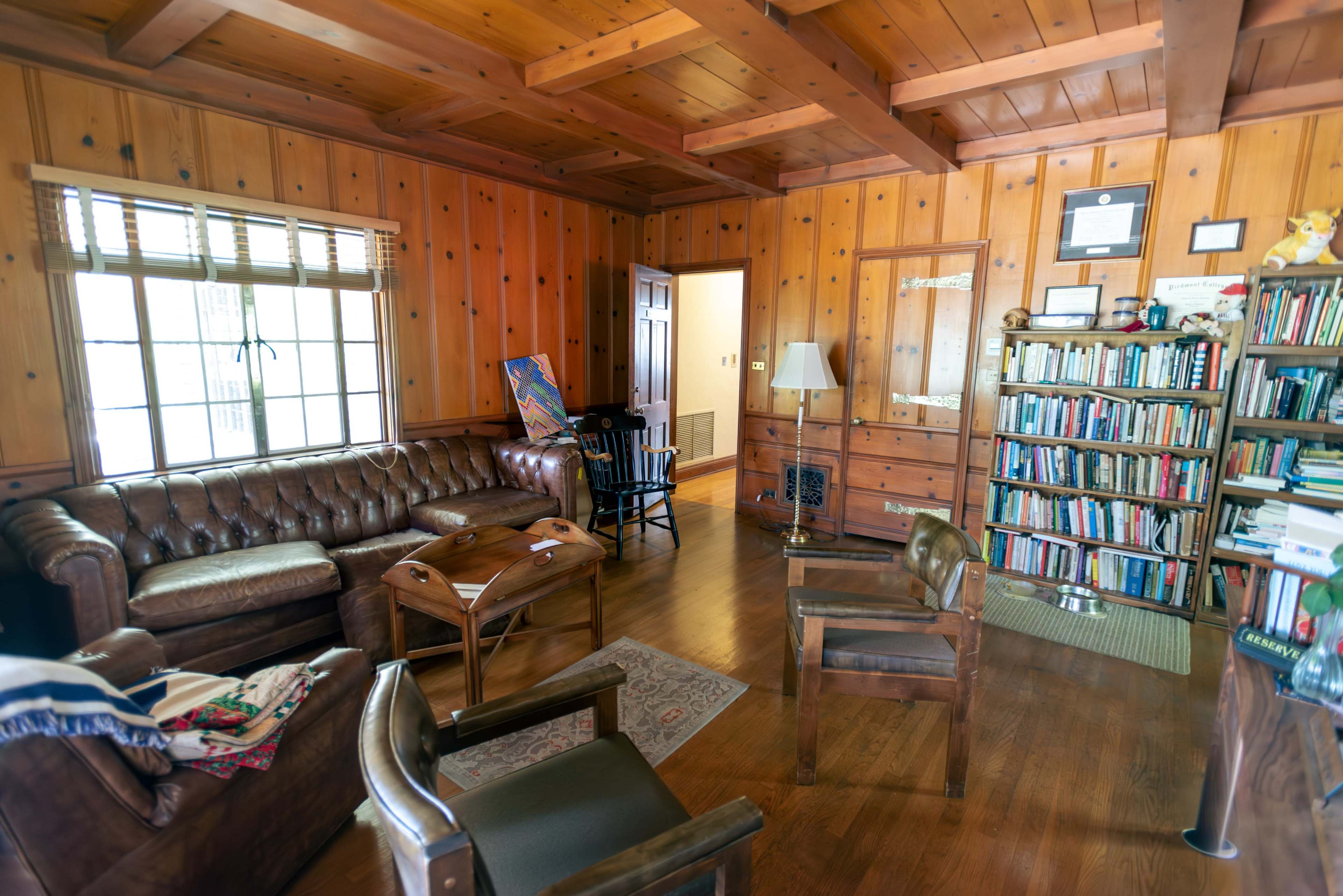 A wooden-paneled living room with a leather couch, a wooden coffee table, and a bookshelf filled with books.