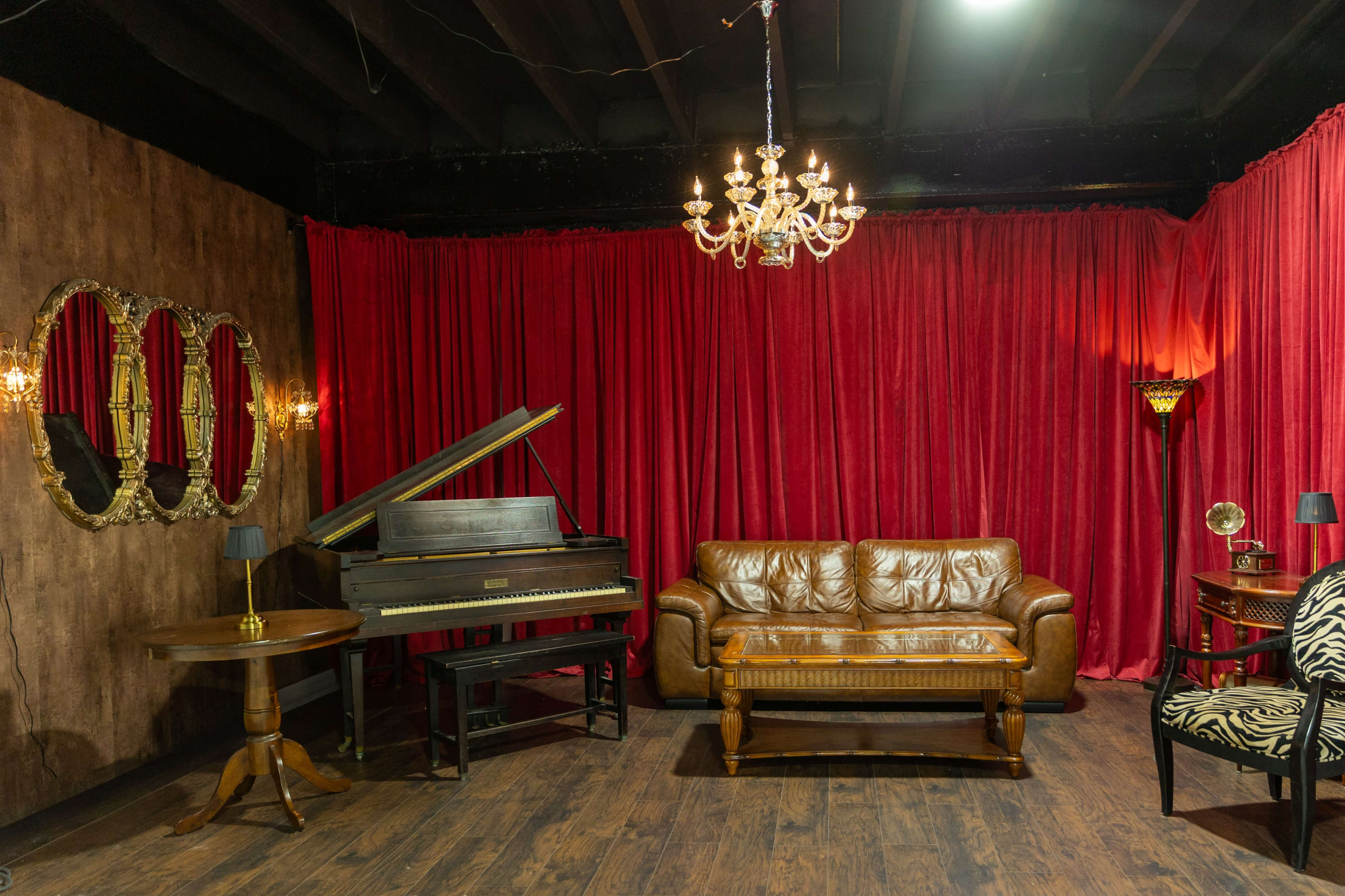 The image shows a cozy room with a grand piano, a brown leather sofa, a wooden table, and red velvet curtains.