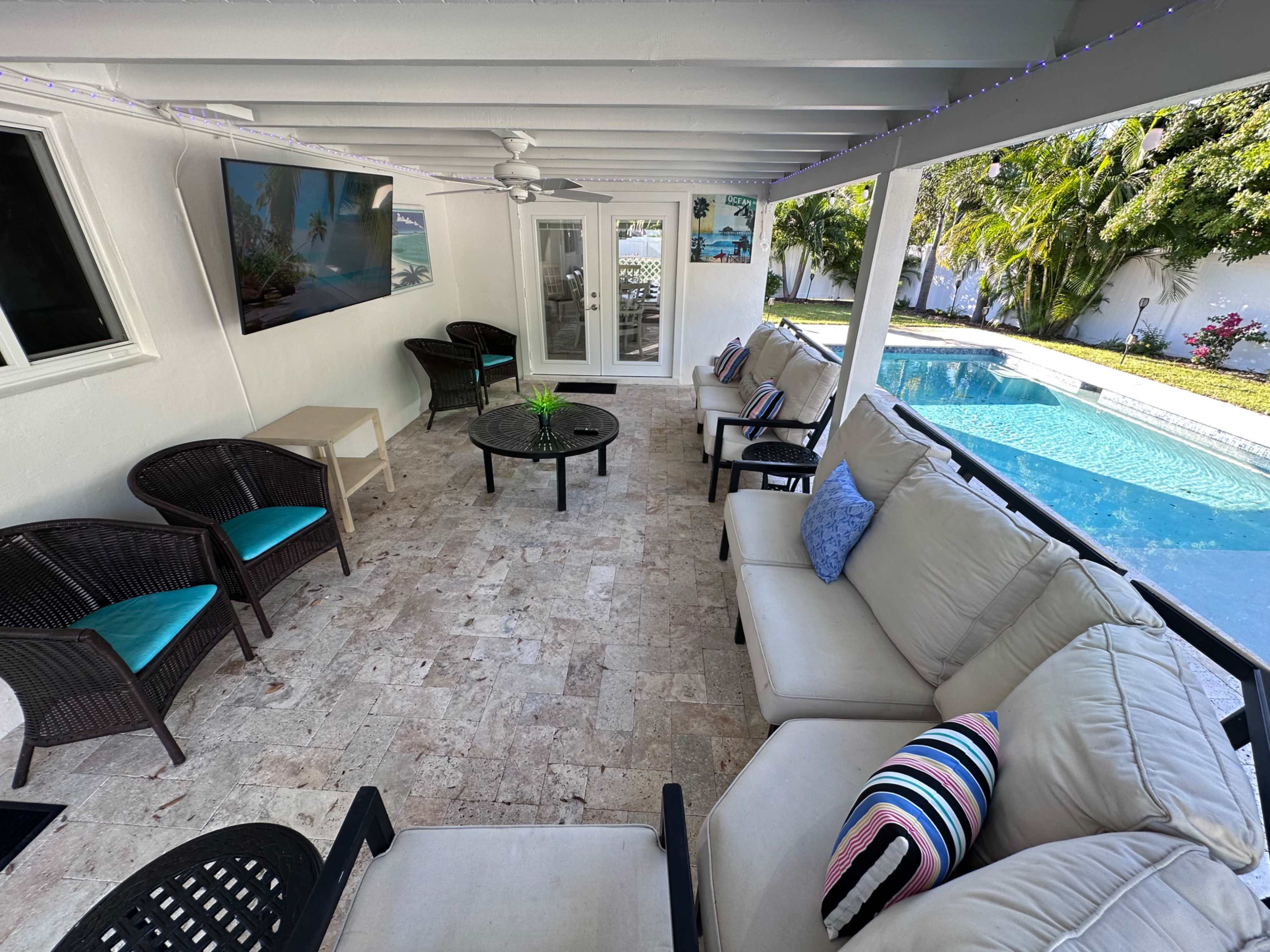 The image shows a covered patio area with seating and a view of a swimming pool in the background.
