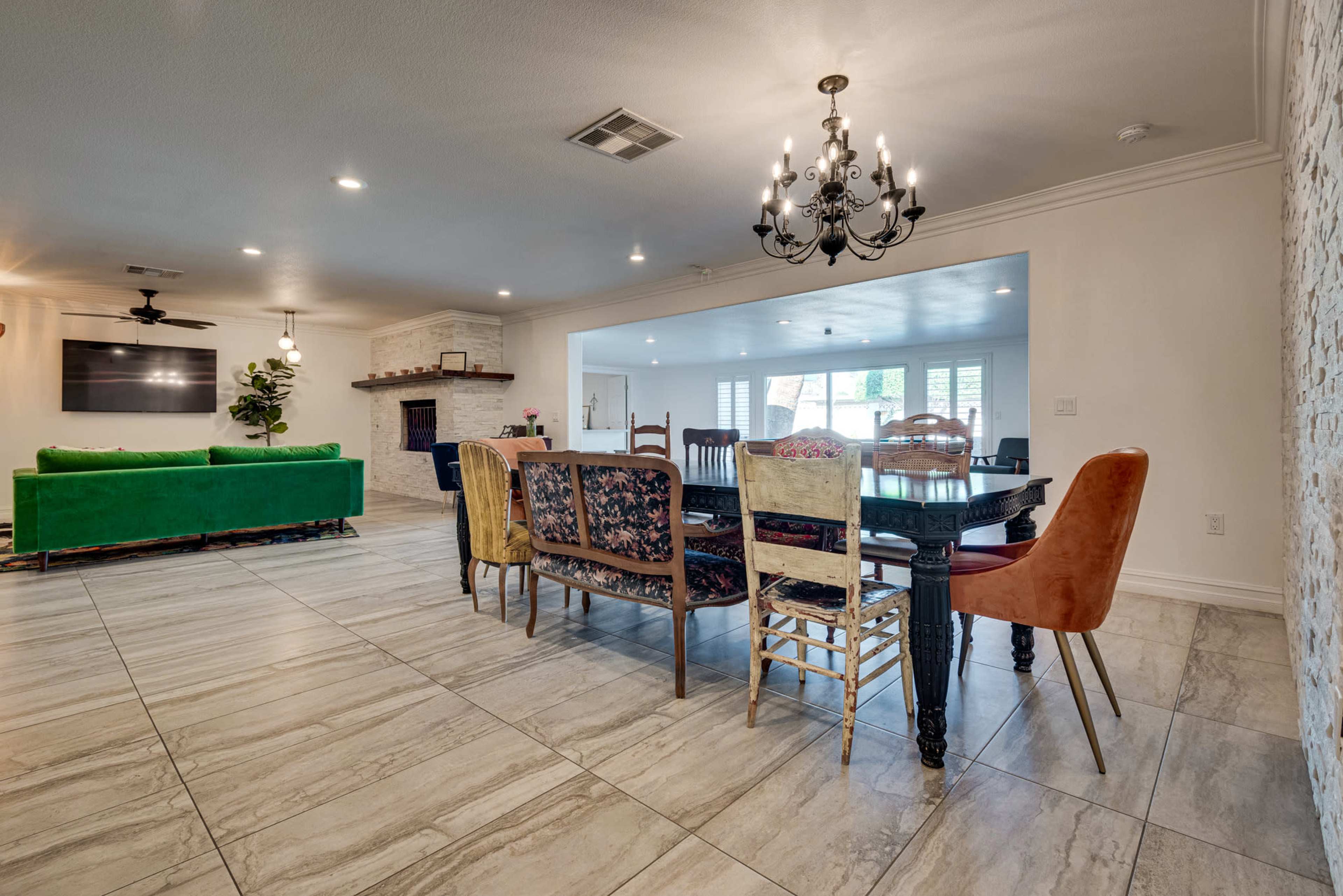A spacious dining area featuring a long table with assorted chairs, a green couch in the background, and a chandelier hanging from the ceiling.