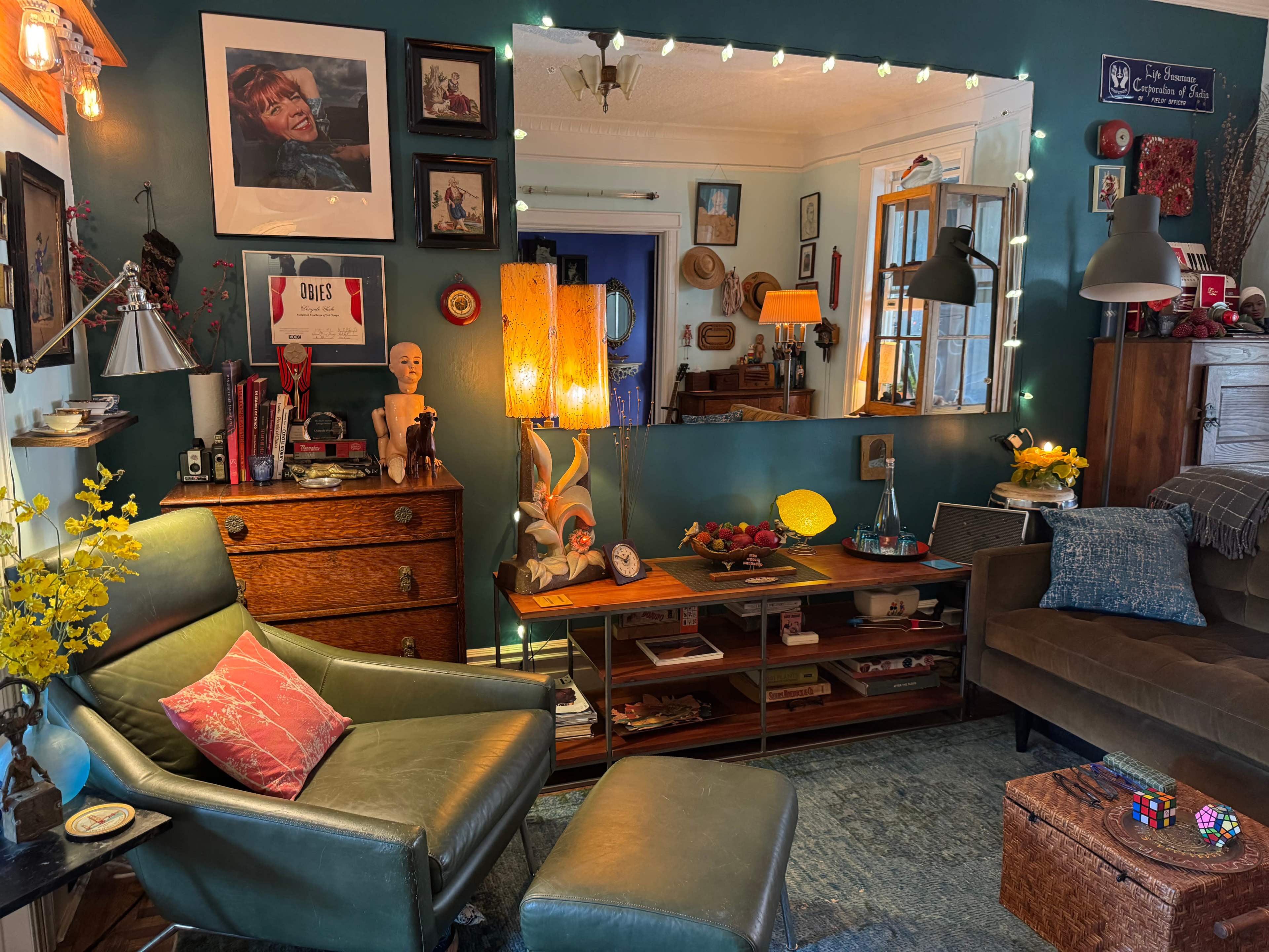 The image features a cozy living room with a green wall, vintage furniture, decorative items, and warm lighting creating an inviting atmosphere.