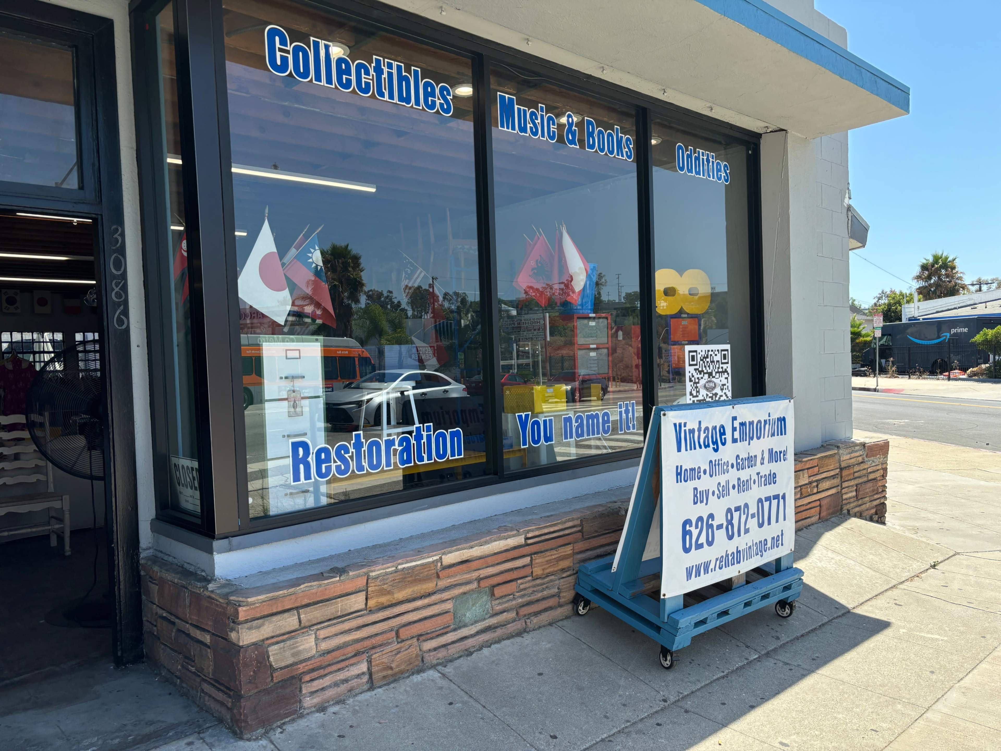 The storefront features large windows displaying items for sale, including collectibles, music, books, and oddities, with a sign advertising a vintage emporium.