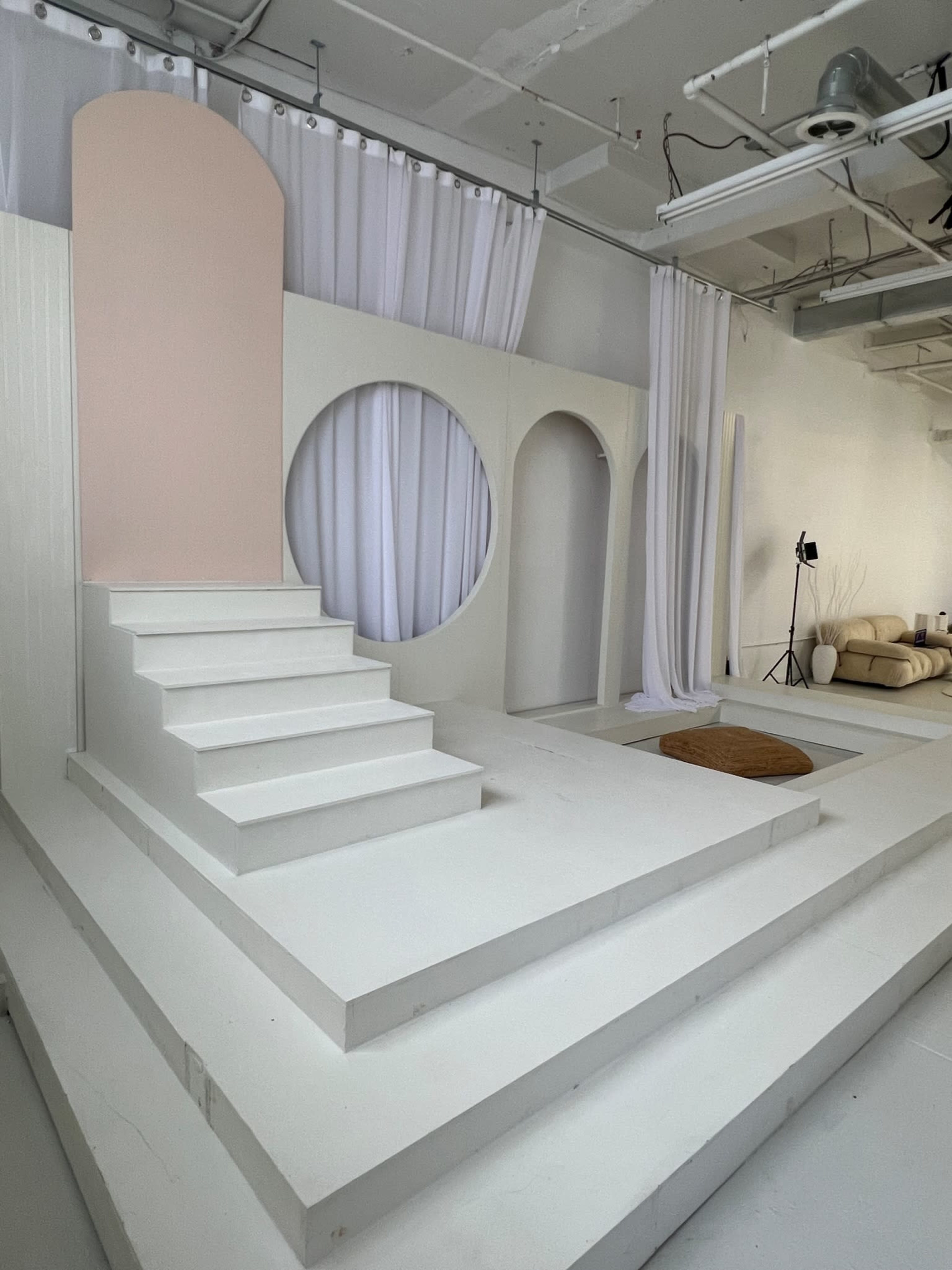A minimalist interior space featuring white steps leading to an archway, with circular and rectangular cutouts and draped fabric in the background.