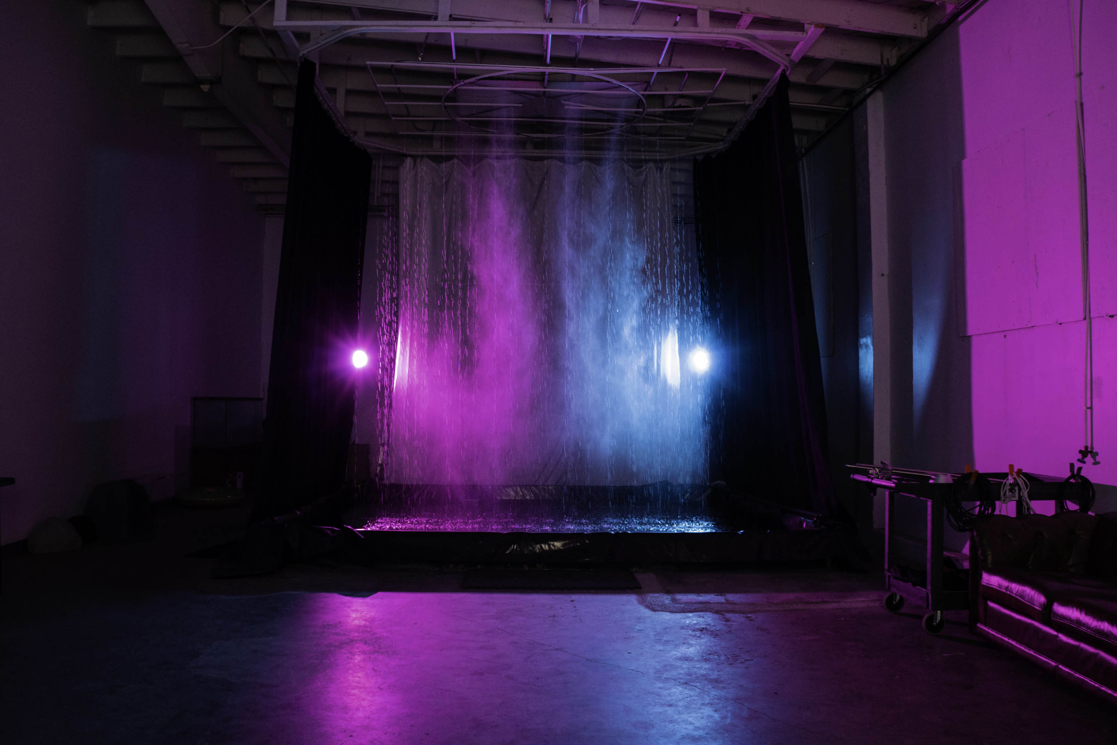 The image shows a room with a large water curtain illuminated by blue and pink lights.