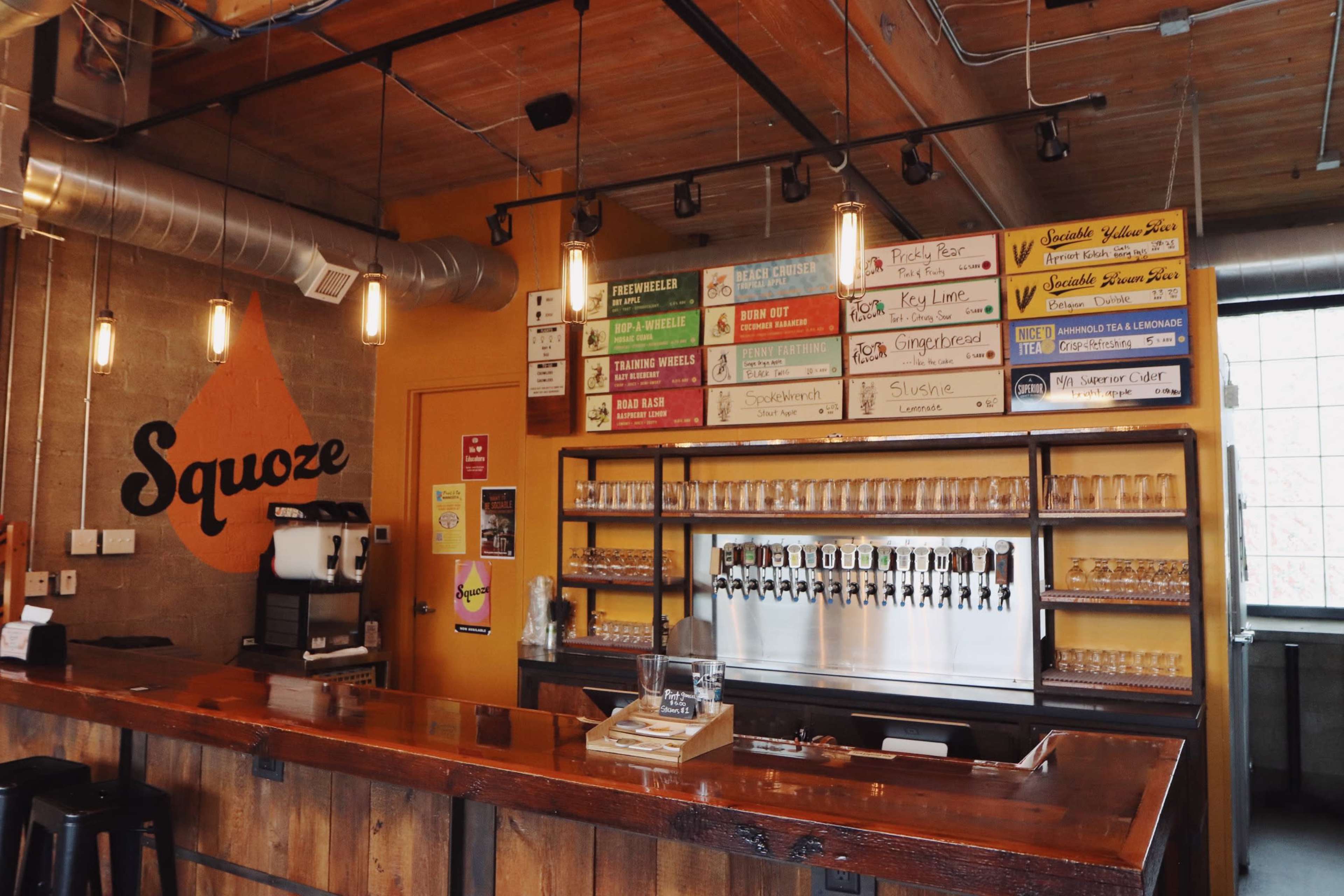 A bar area with a wooden counter, a wall featuring a menu of beverages, and multiple beer taps.