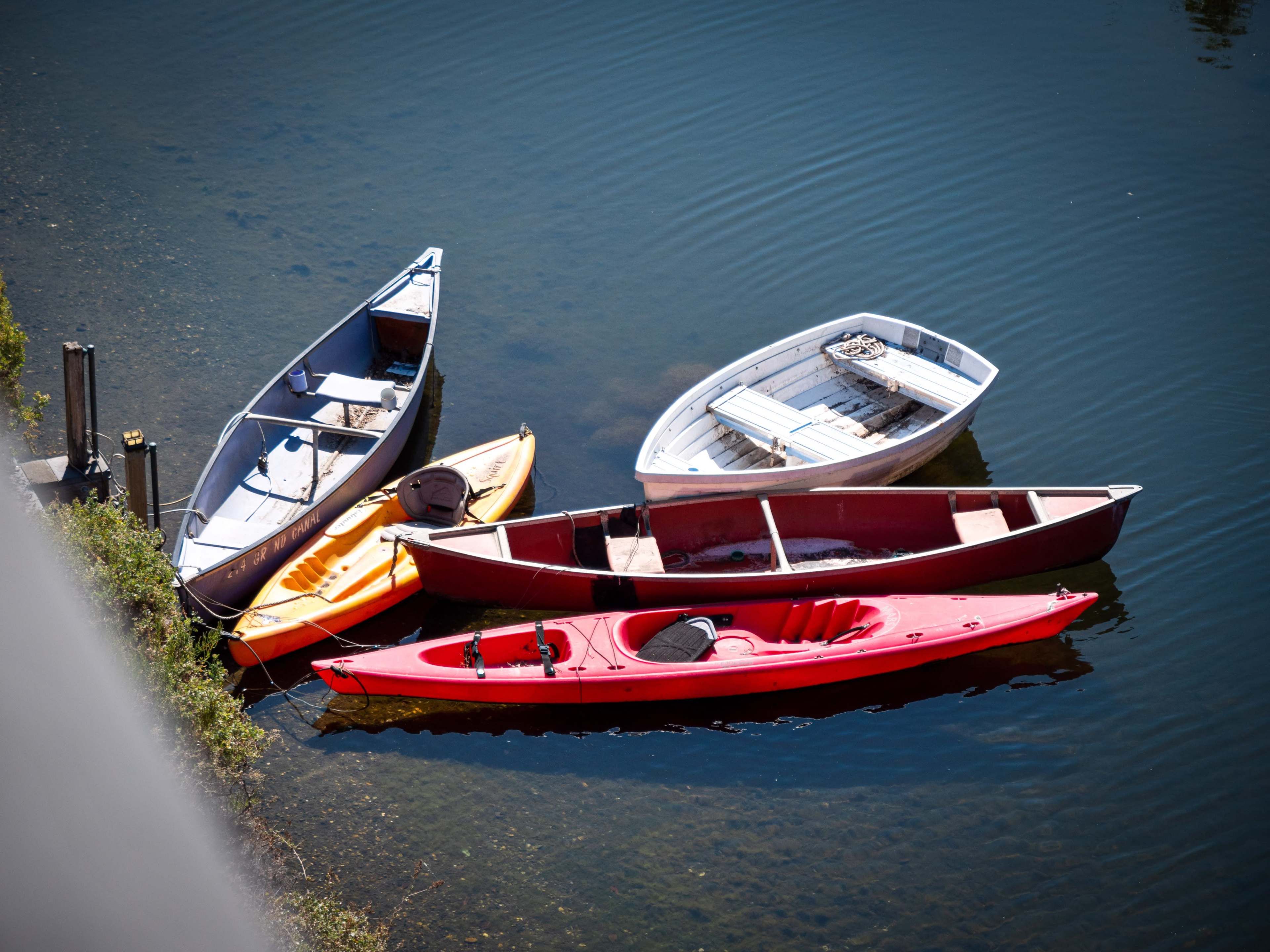 Four boats, including a red kayak and a yellow canoe, are docked on still water.