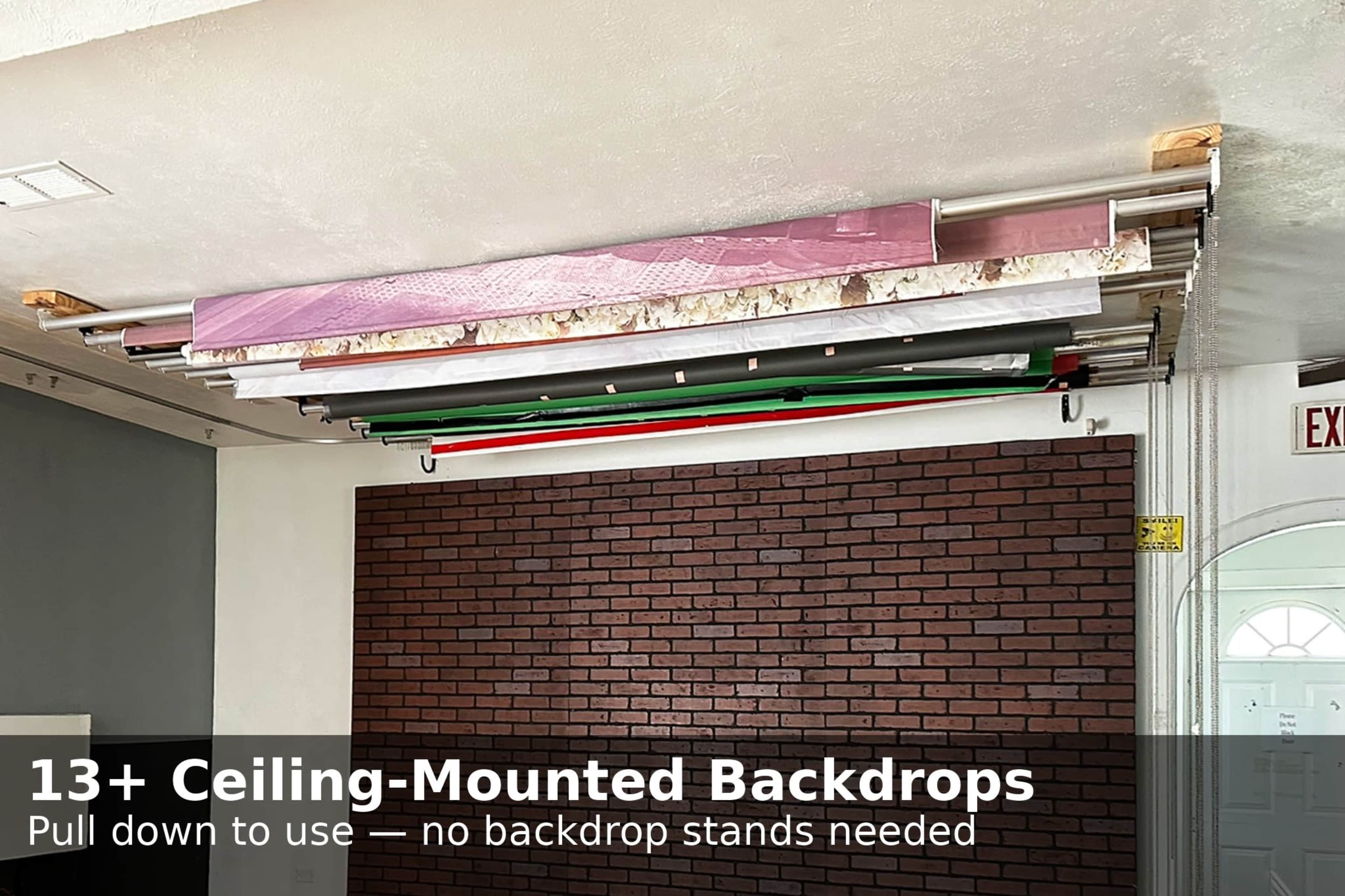 The image shows multiple ceiling-mounted backdrop rolls arranged horizontally above a brick wall, providing an easy pull-down option for backgrounds in a studio setting.