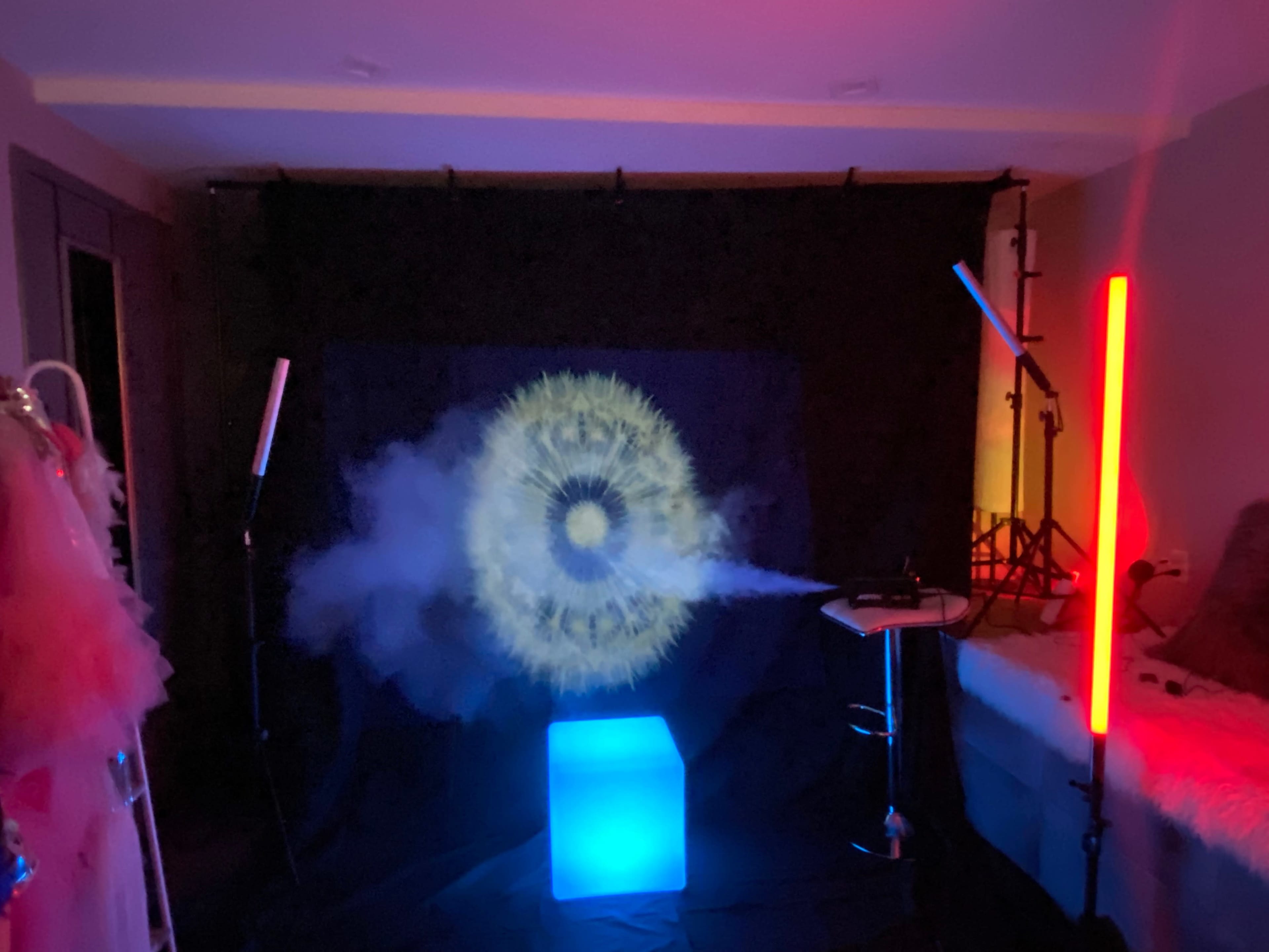 A dimly lit room with a circular light pattern projected onto a black backdrop, accompanied by colored lighting and a smoke effect, creating a visually striking scene.
