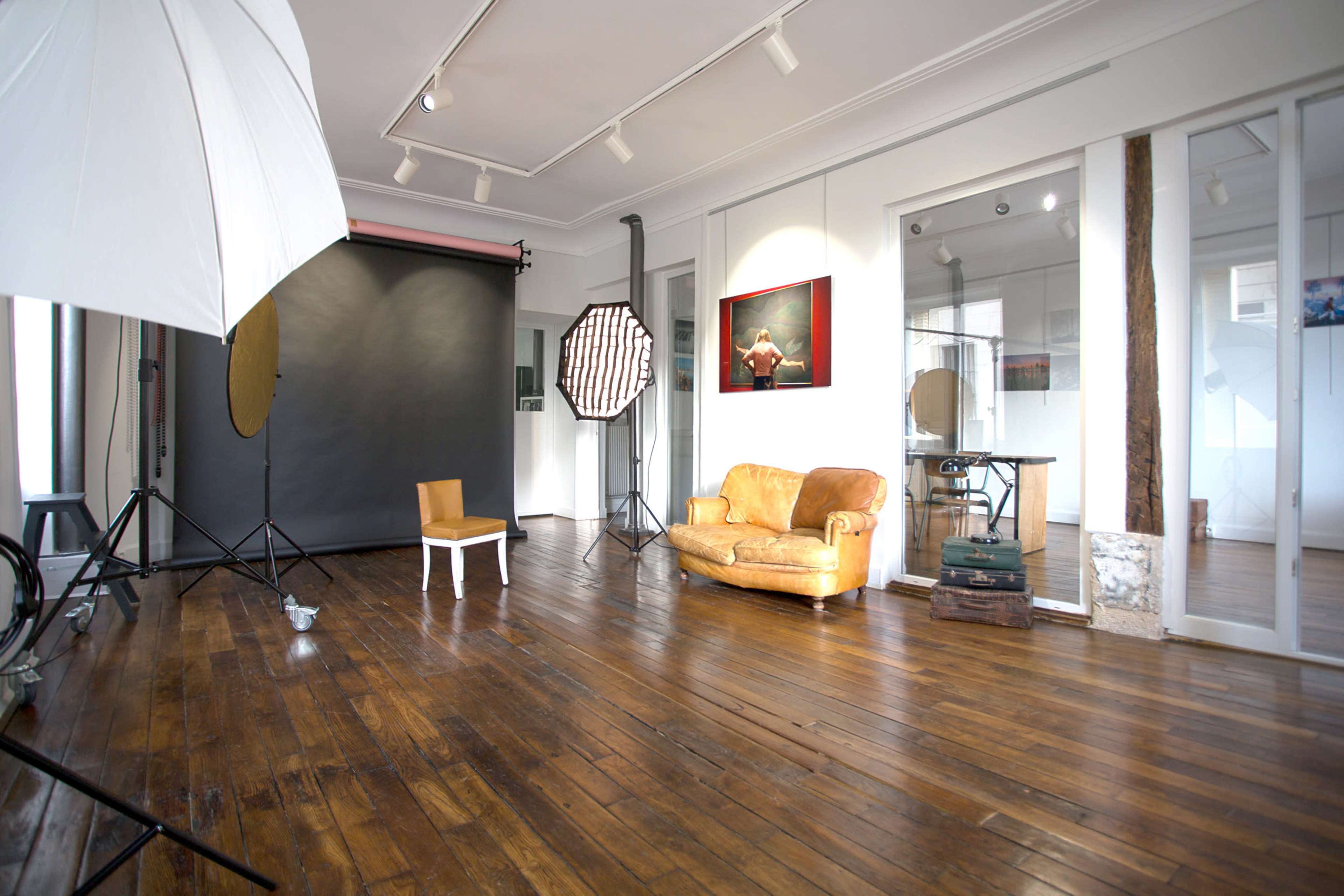 A photography studio with a wooden floor, a sofa, a chair, and various lighting equipment set up around a dark backdrop.