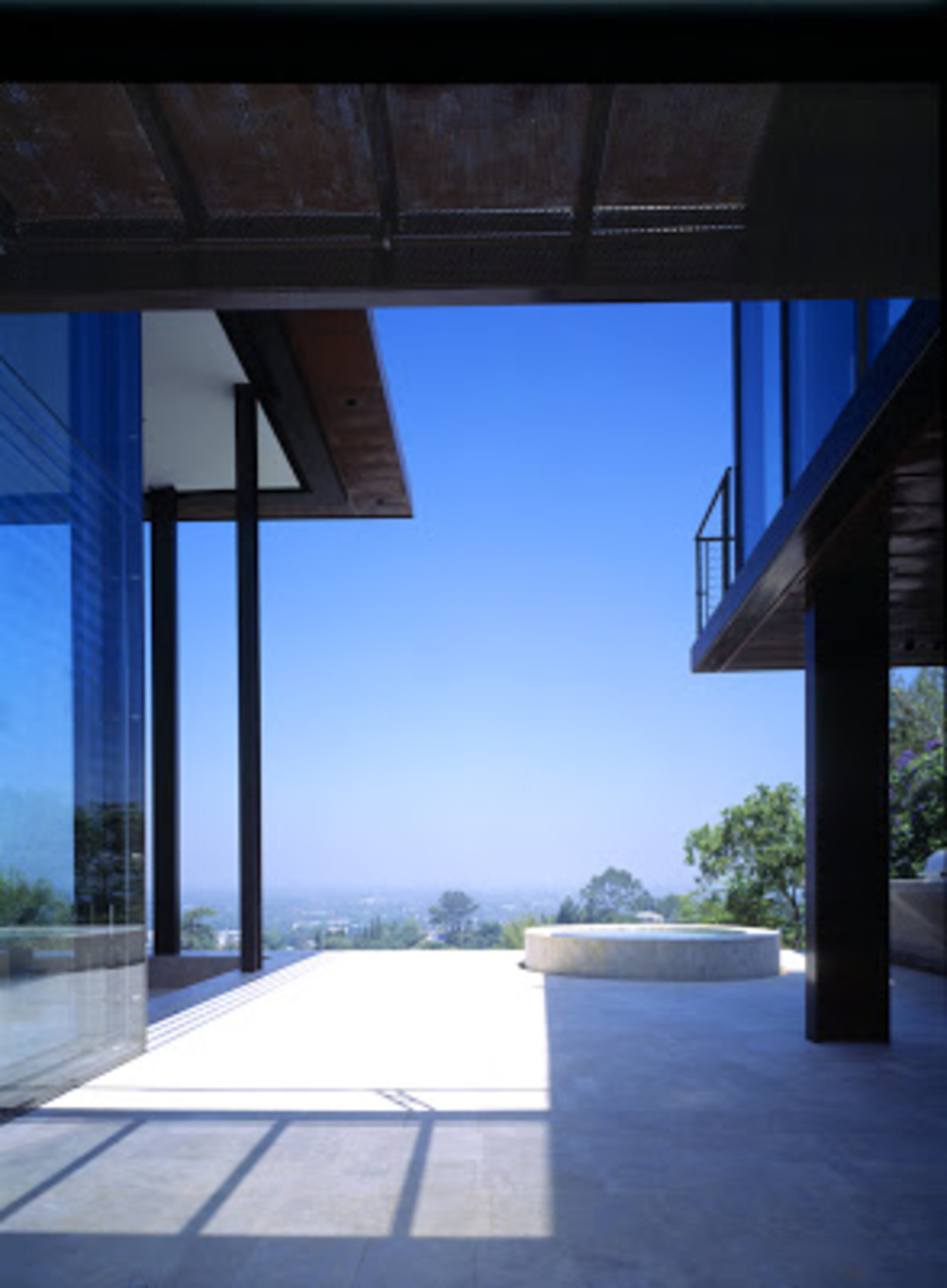 A modern, open architectural space with large glass windows overlooking a blue sky and distant landscape.