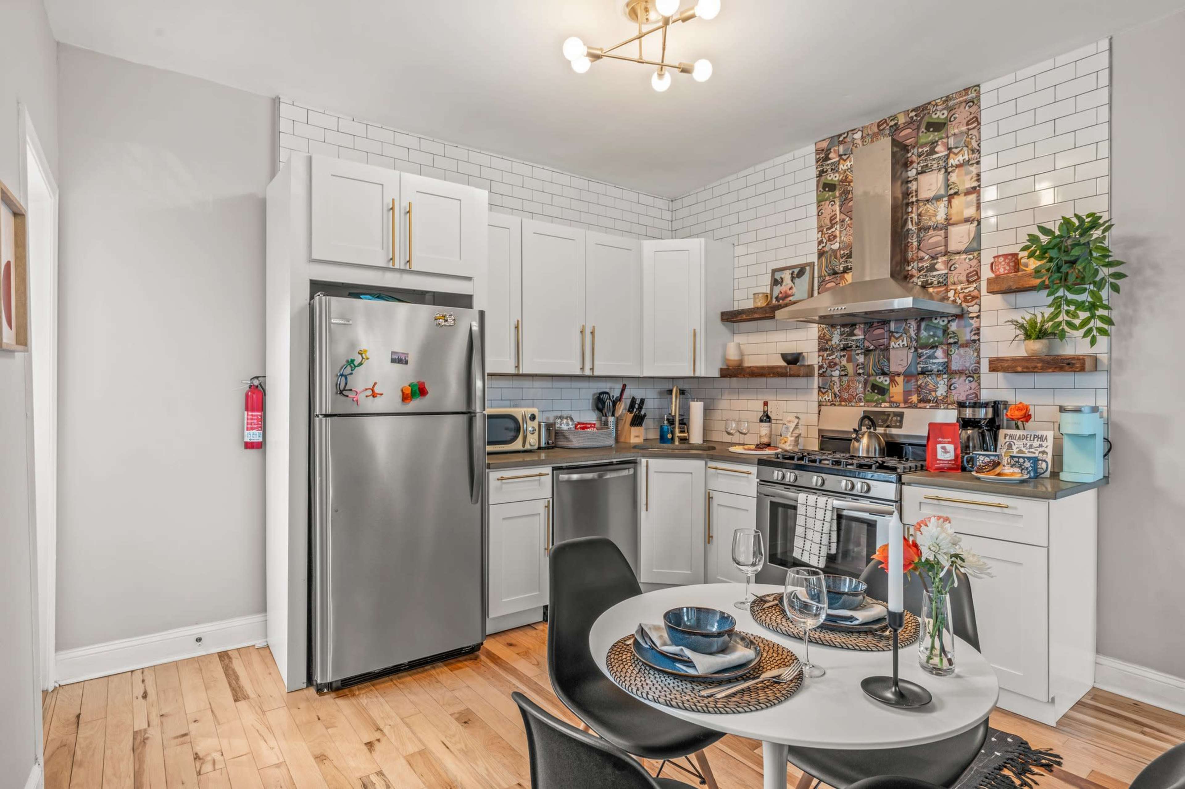 The image shows a modern kitchen featuring stainless steel appliances, white cabinetry, and a round dining table set for two.