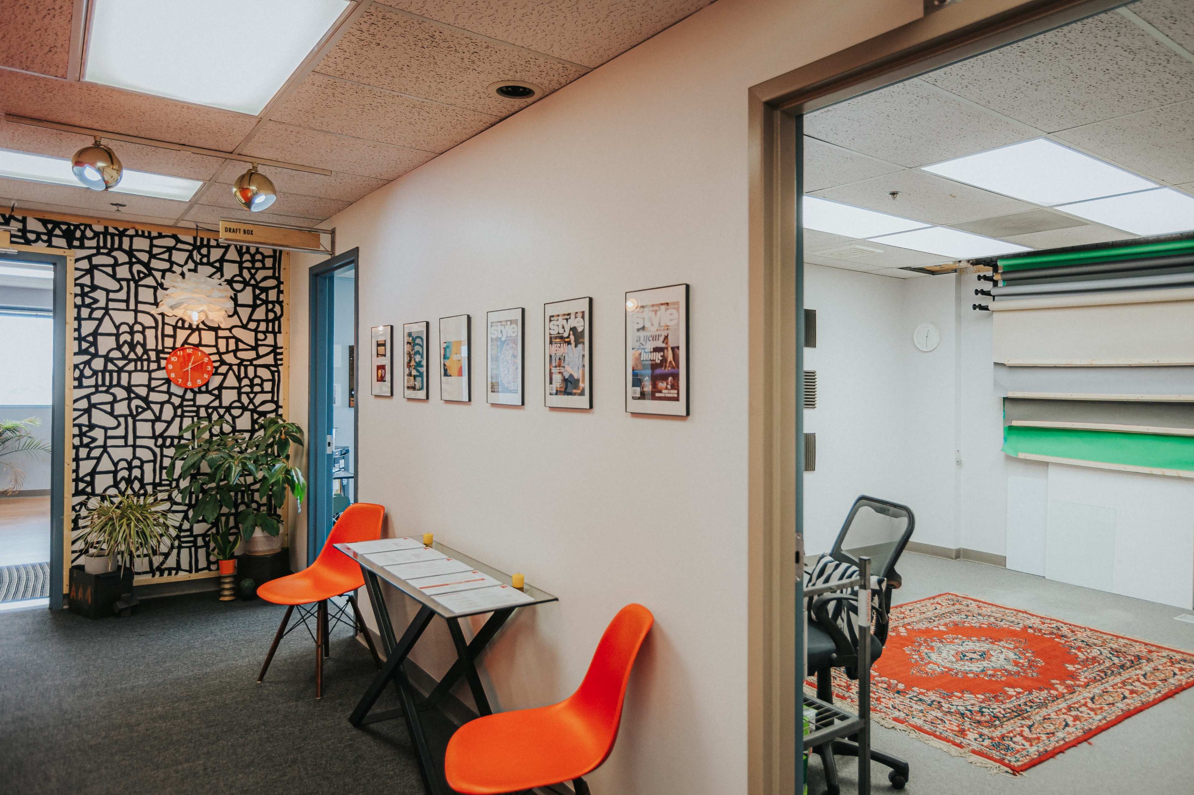A hallway features orange chairs and framed photographs on the wall, leading to a room with studio backdrops and a patterned rug.