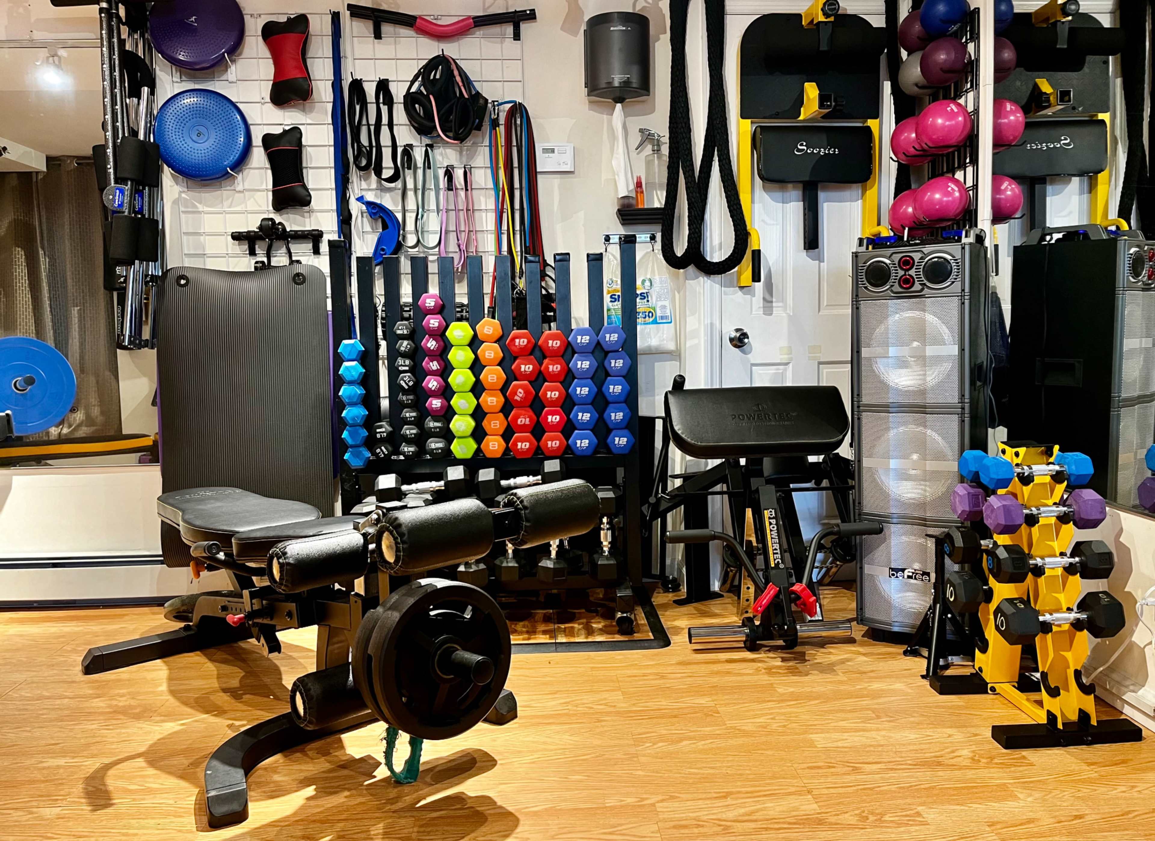 A well-equipped home gym featuring various weights, exercise machines, resistance bands, and fitness equipment organized on the walls.