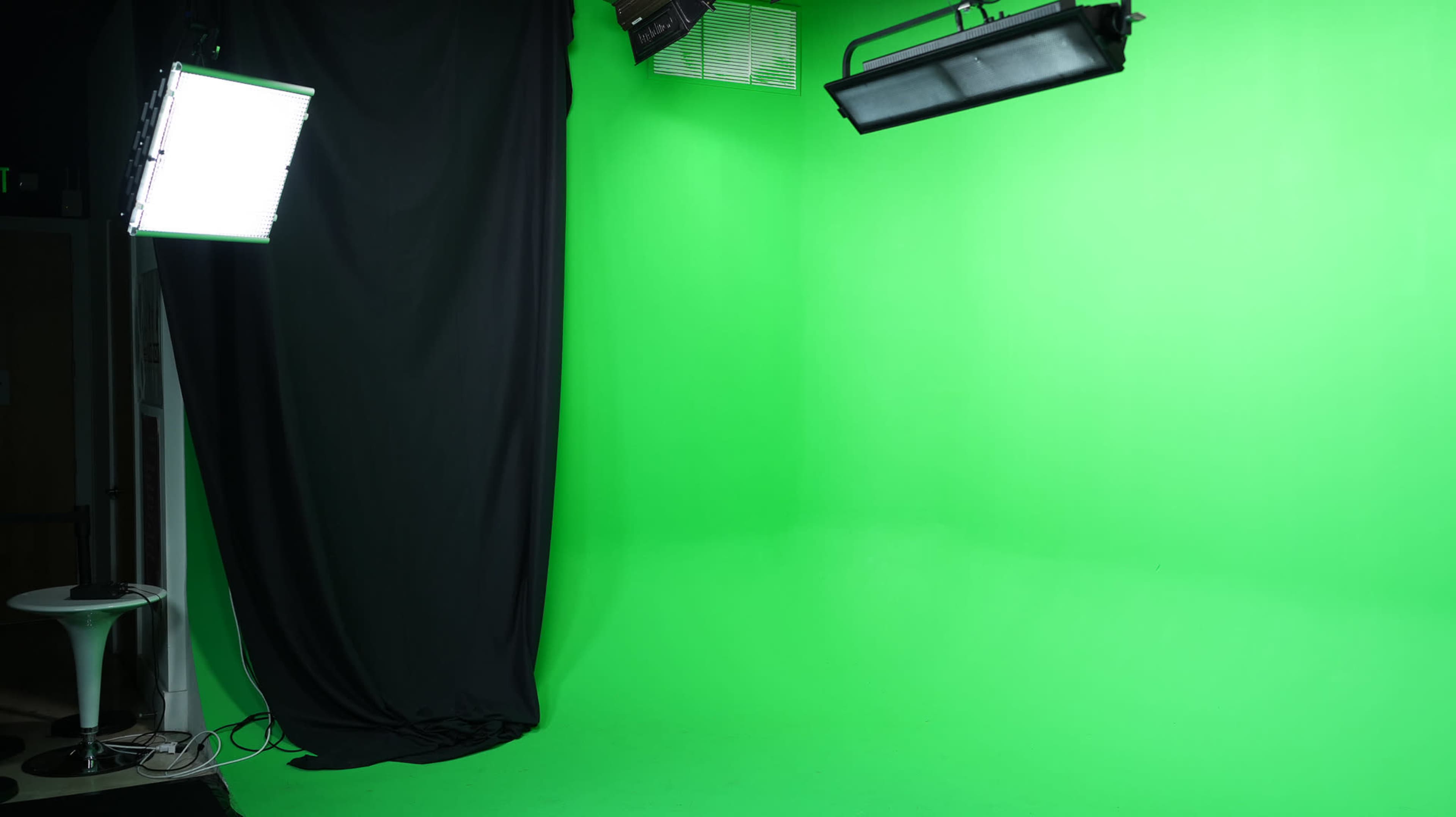 A photography studio with a green backdrop, black drapes, and overhead lights.