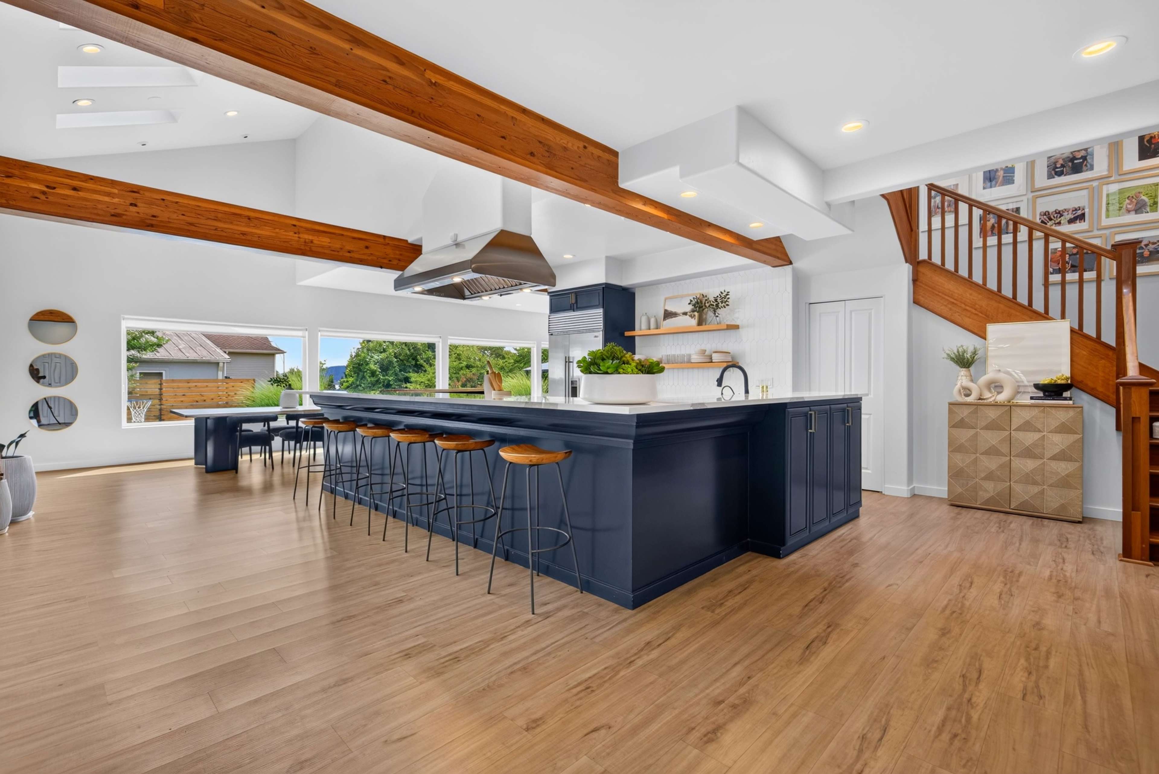 The image shows a modern kitchen with a large island, dark blue cabinetry, and exposed wooden beams overhead.