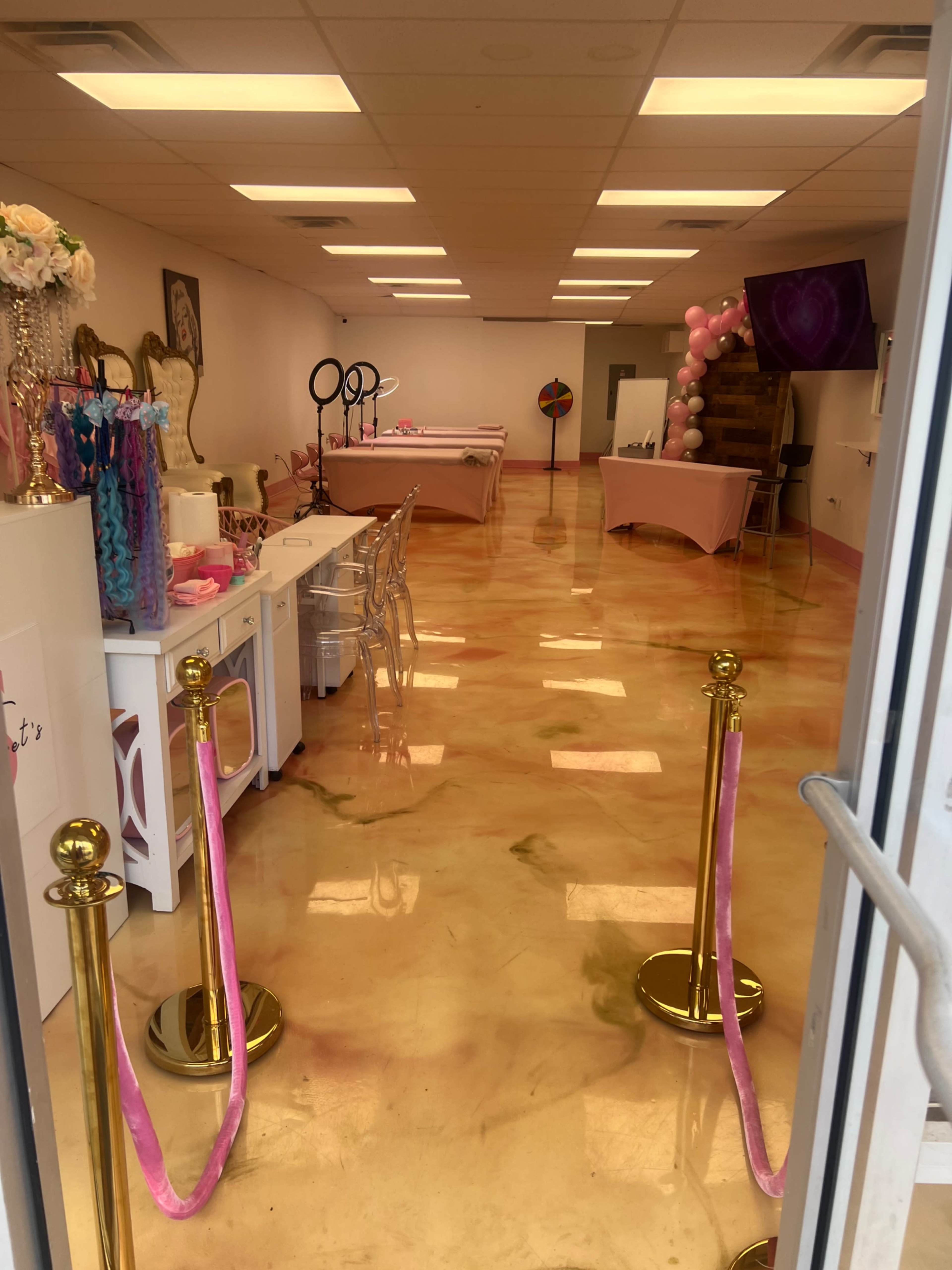 The image shows a brightly lit event space with a polished floor featuring swirls of pink and orange, lined with golden stanchions and pink rope barriers.