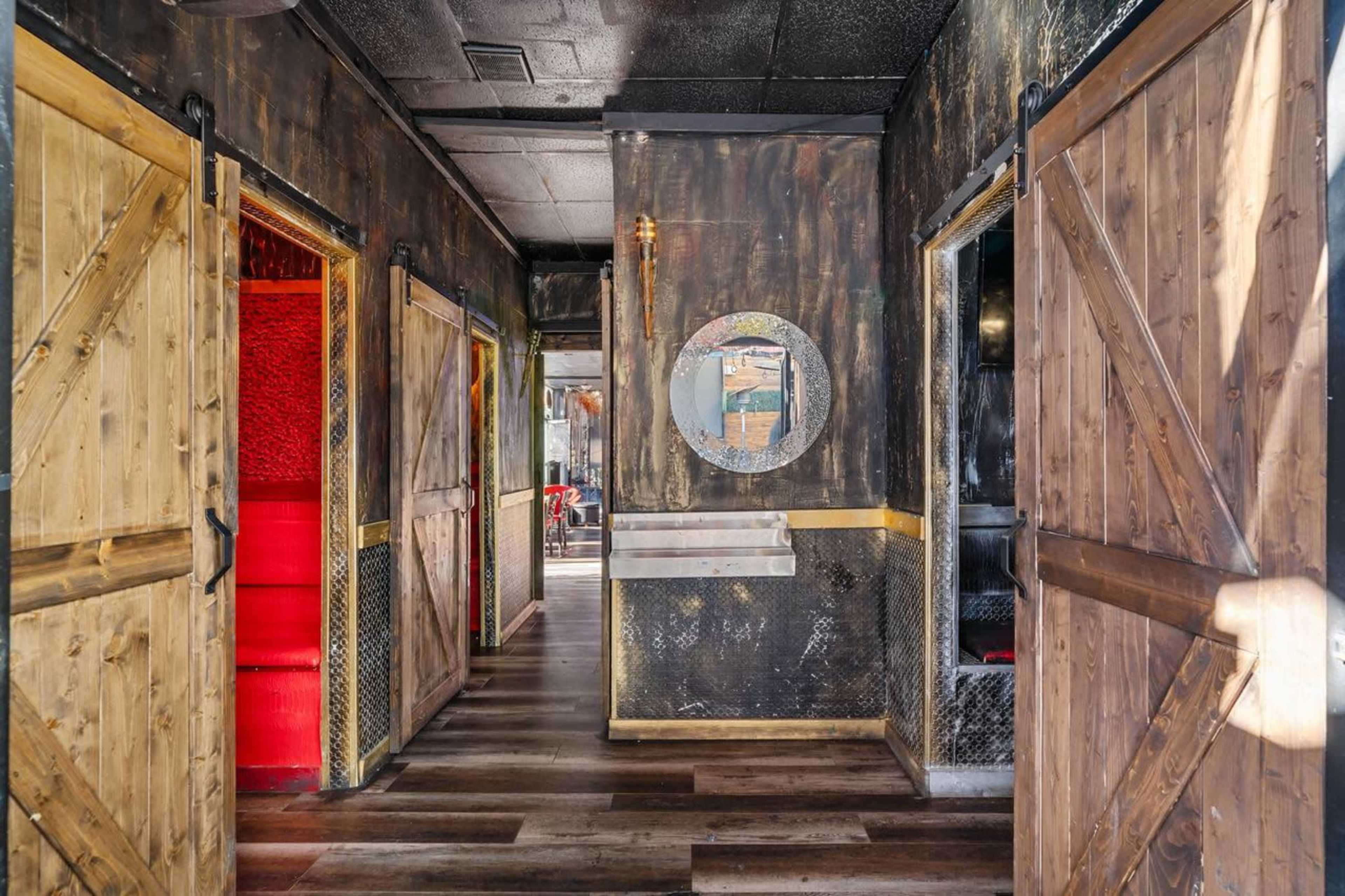 The image shows a hallway with wooden doors on either side, leading to rooms painted in dark tones, and a circular mirror on the right wall.