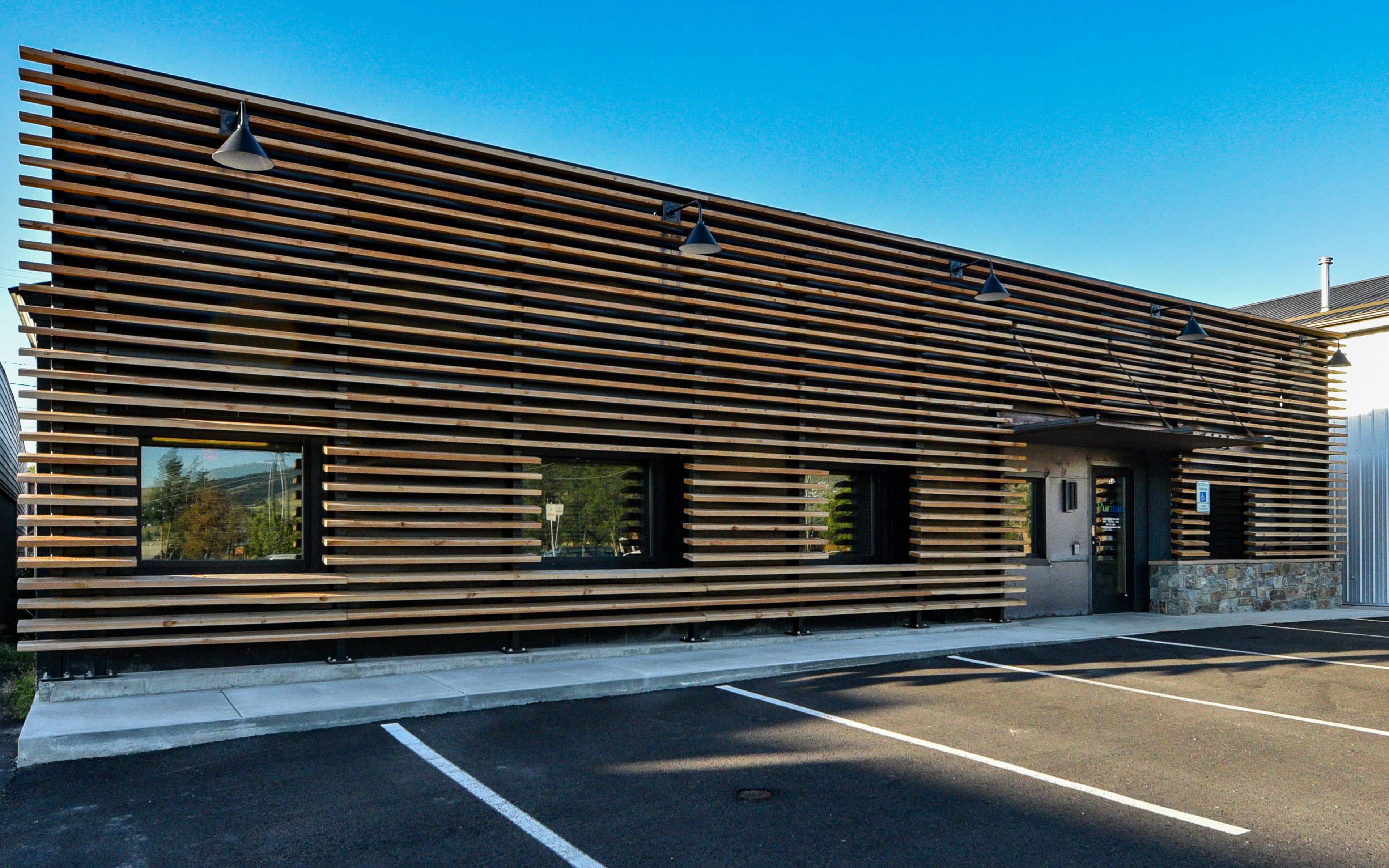 A modern building with a facade made of horizontal wooden slats, situated in a parking lot.