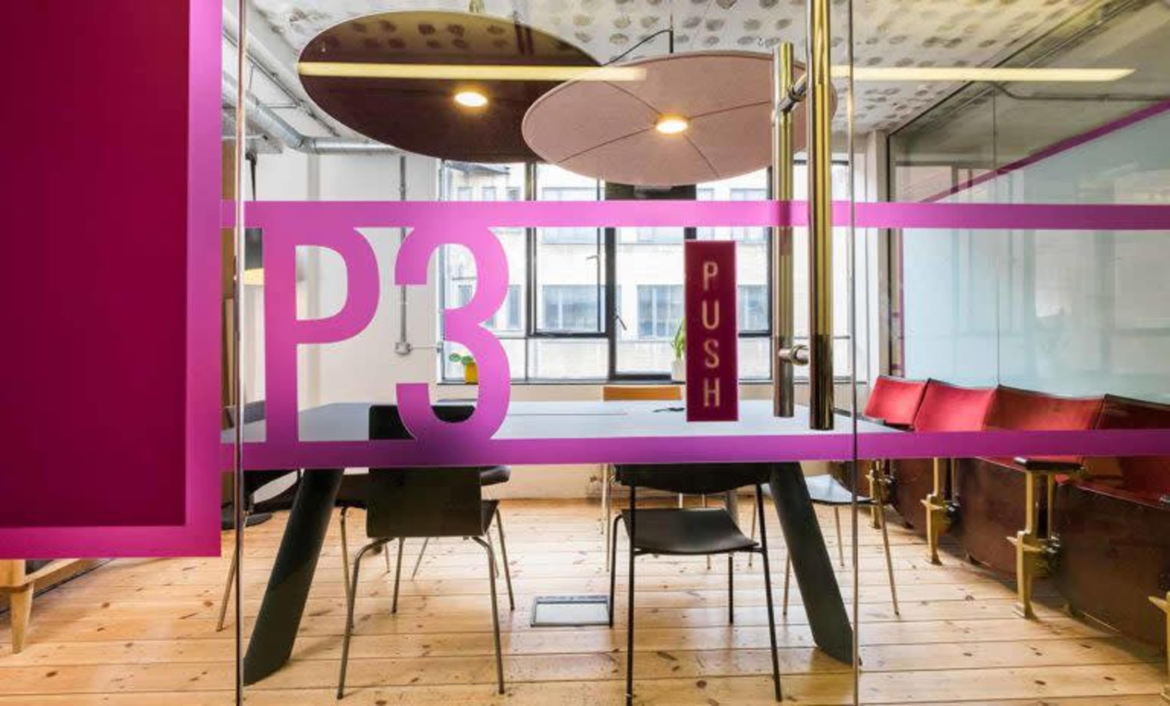 A modern conference room features a glass wall with the letters "P3" and the word "PUSH" displayed, along with a large table and red chairs.