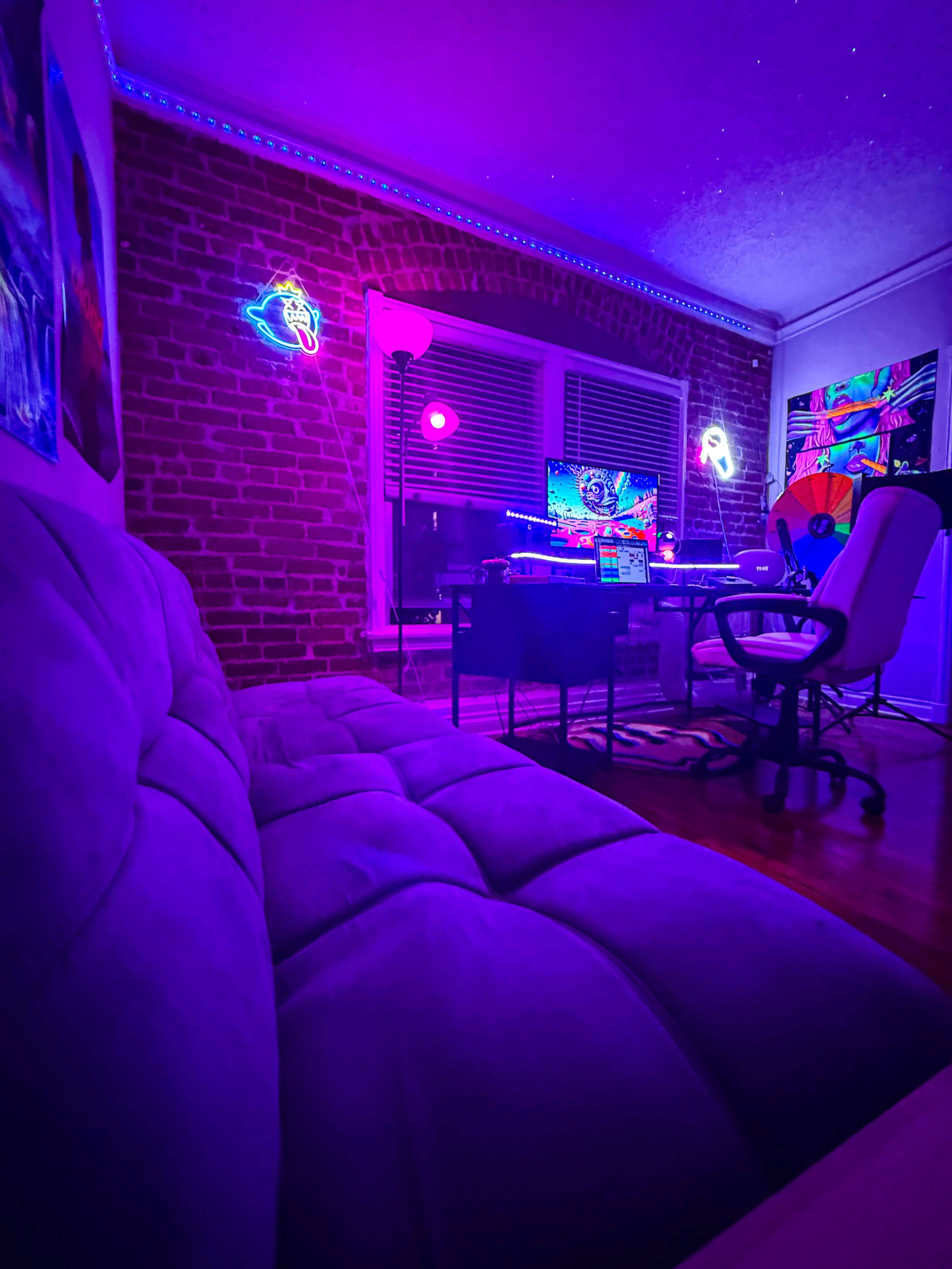 The image shows a modern gaming setup in a dimly lit room with purple lighting, featuring a desk, computer, and neon decorations on the walls.